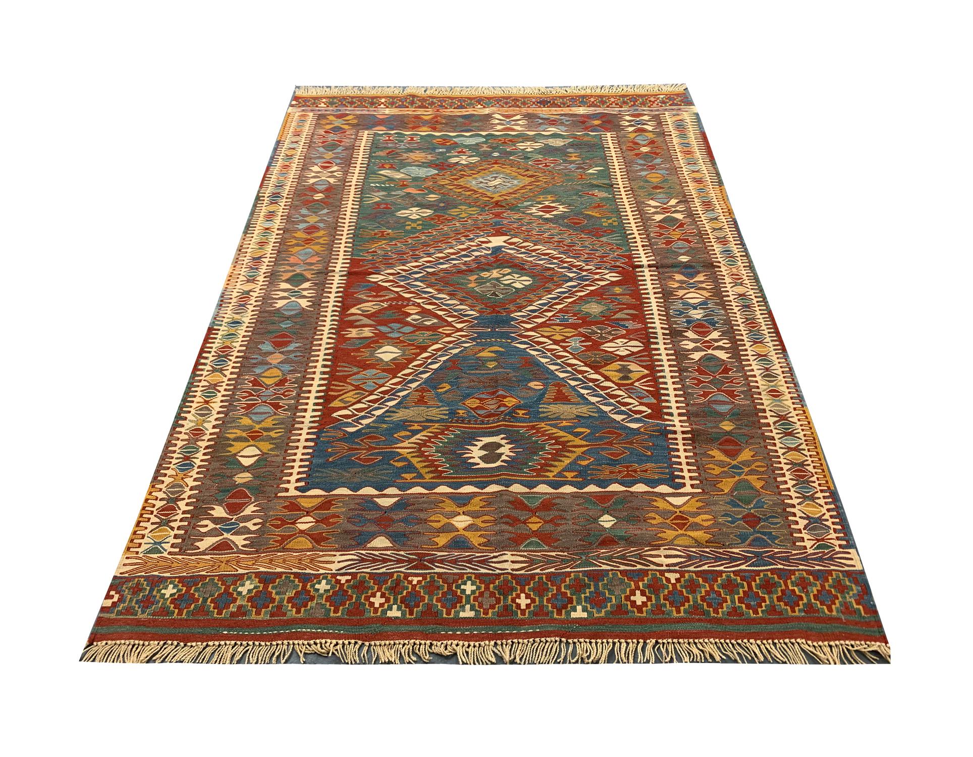 This elegant handwoven kilim rug is a vintage Turkish rug woven in the 1980s. The design features a tribal design with diamonds and medallions woven throughout with red, blue, green, and yellow accents. A repeat pattern border has then framed this.