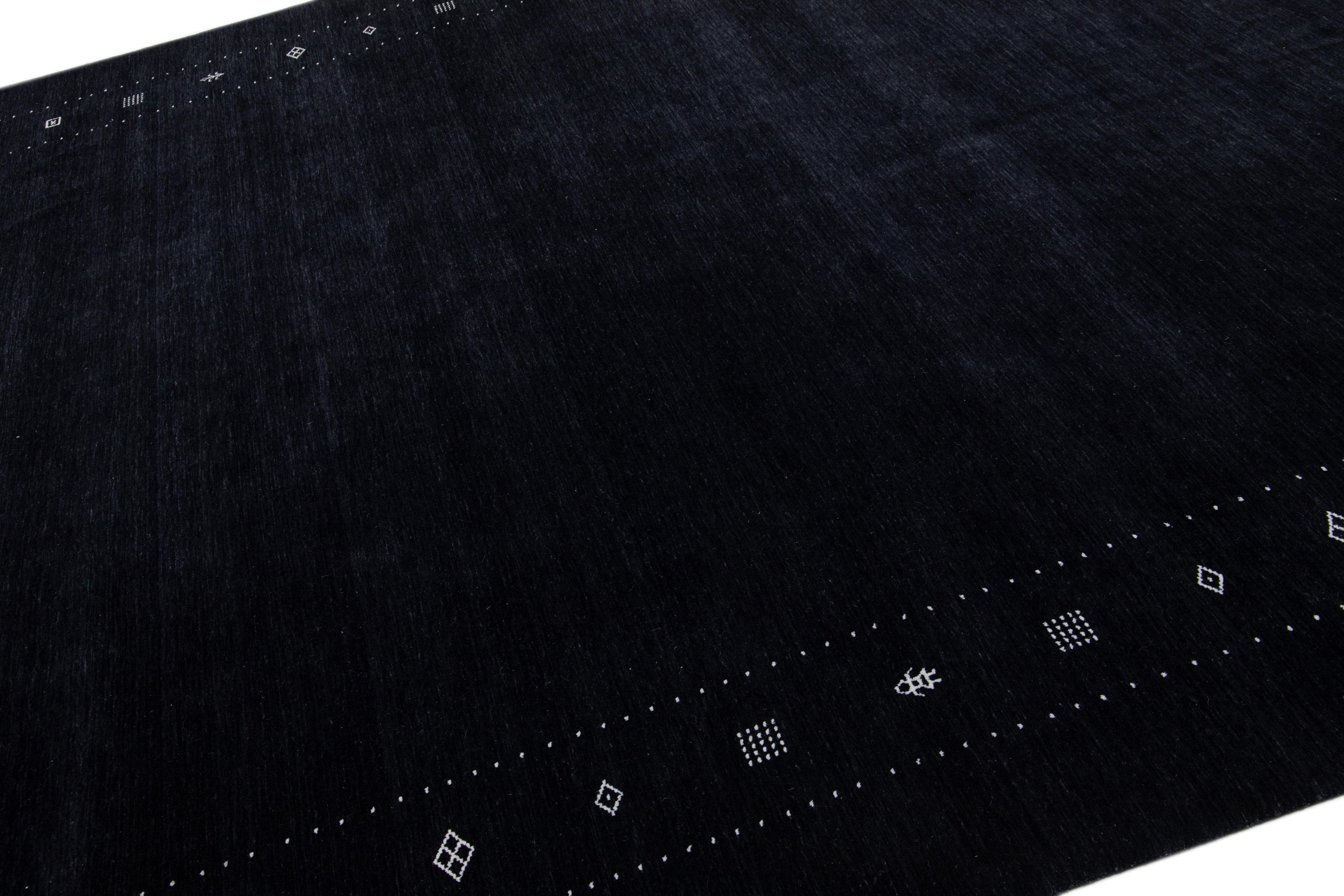 A stunning modern Gabbeh-style hand-woven wool rug boasting a black color field and exquisite white minimalist design. 

This rug measures: 10'1