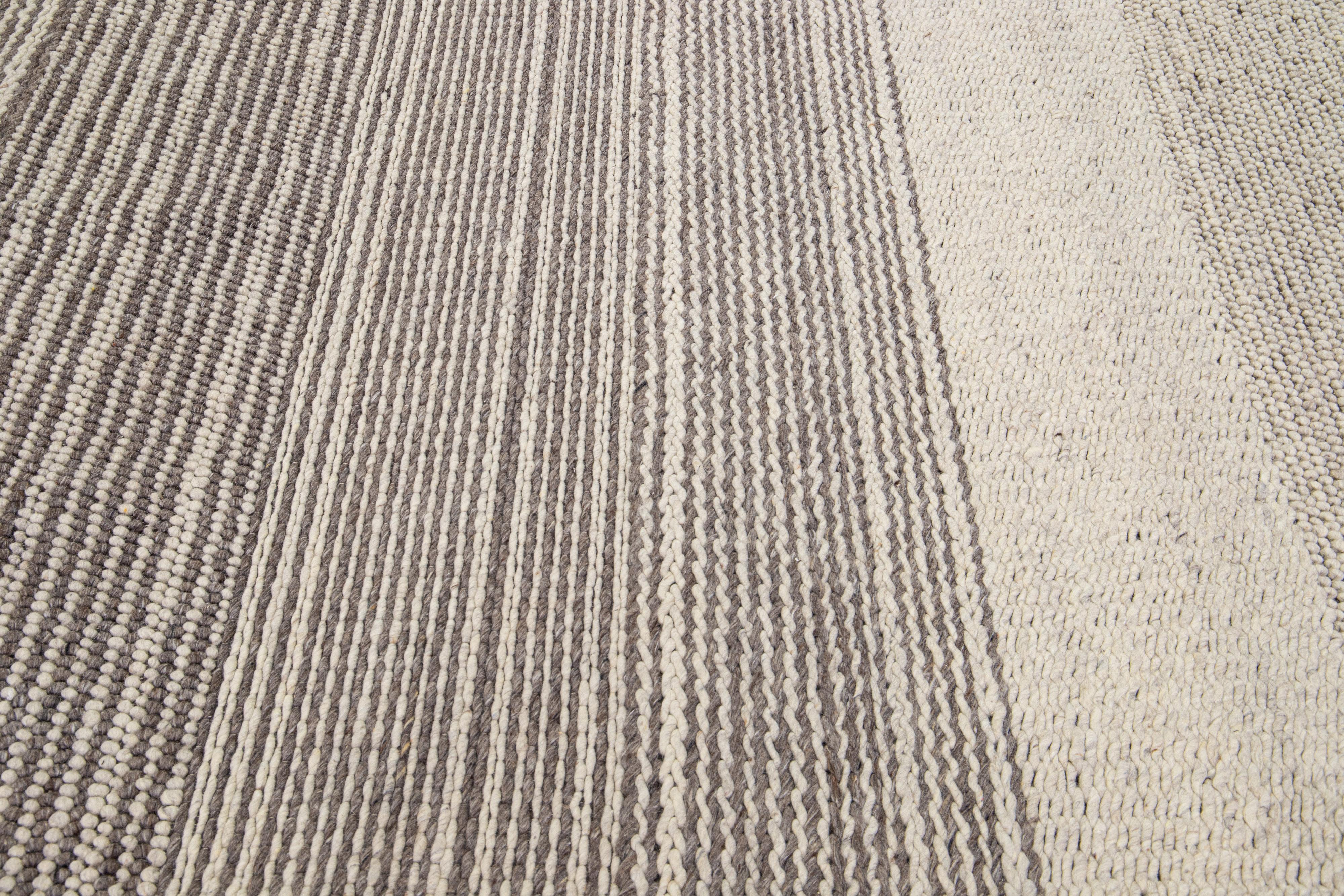 Dieser handgeknüpfte Wollteppich zeichnet sich durch eine moderne Ästhetik im Textur-Stil aus, mit einem klassischen beigen Feld und minimalistischen grauen Streifen.

Dieser Teppich misst: 8' x 10'.

Unsere Teppiche werden vor dem Versand