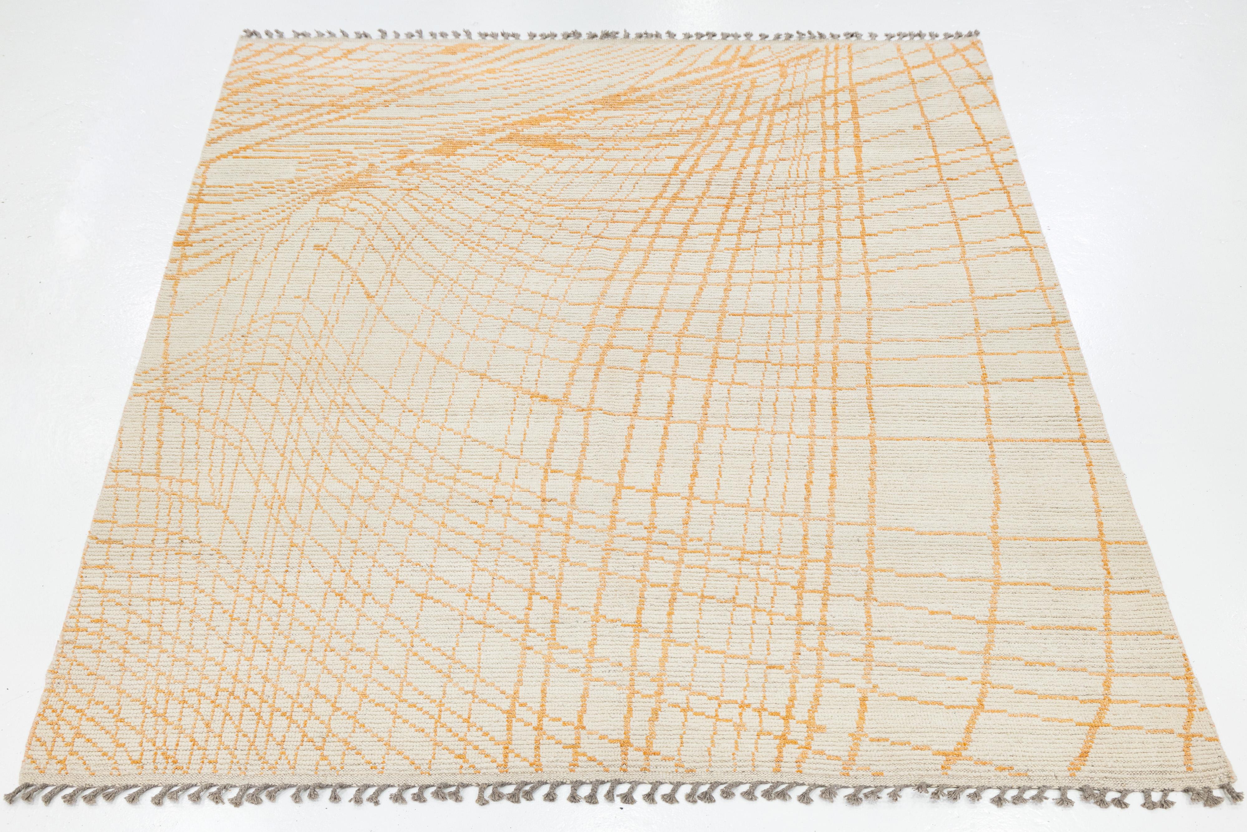 This modern Moroccan-style wool rug features a flowing grid of orange lines over a soft beige field, evoking topographic movement and artisanal charm. Handwoven with fringe accents, its abstract geometry adds warmth and sophistication to minimalist,