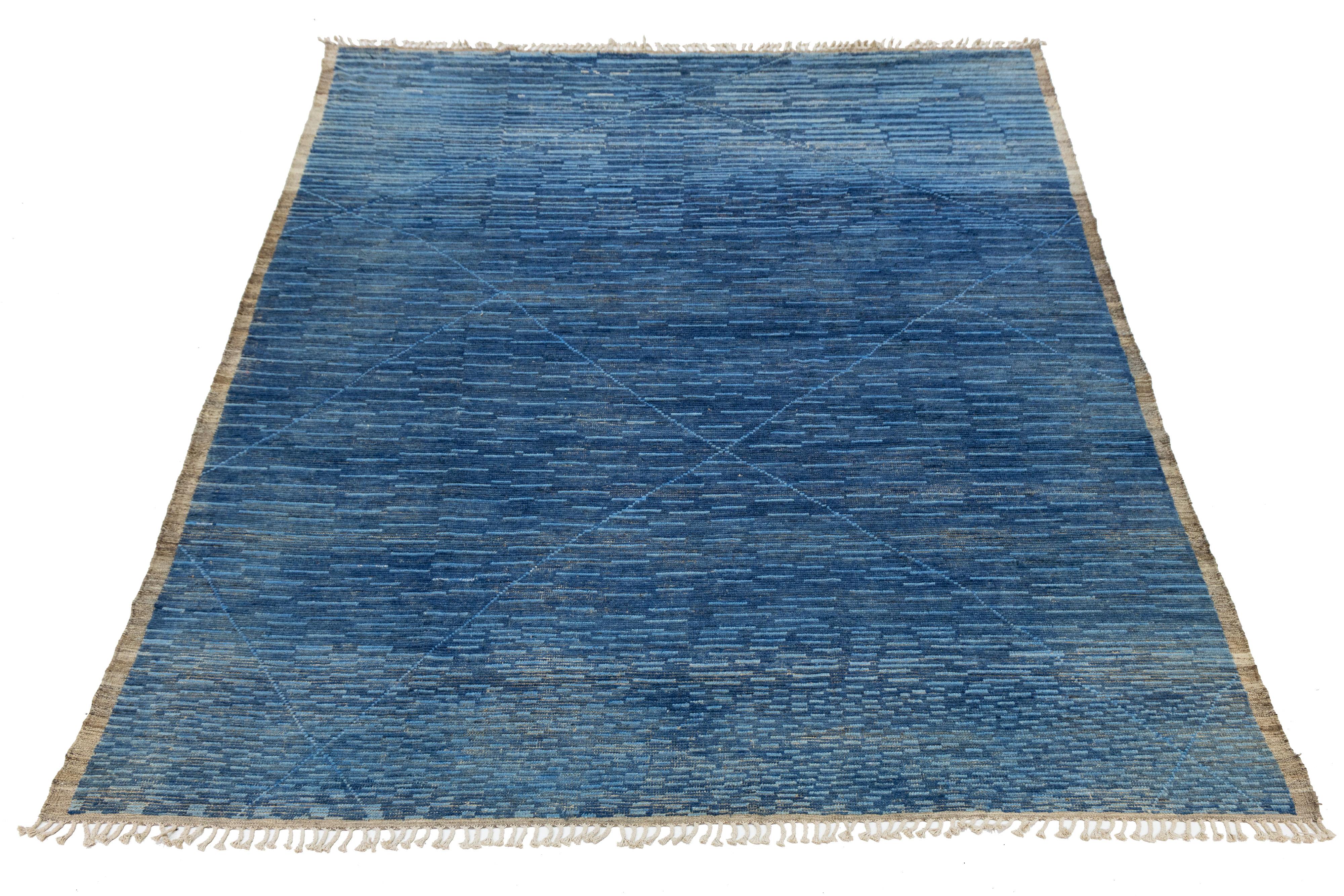 Dieser atemberaubende, handgefertigte Wollteppich ist ein Beispiel für zeitgenössisches marokkanisches Design mit seinem auffälligen braunen und beigen Hintergrund. Seine modernen geometrischen Muster in einem kräftigen Blauton sorgen für eine