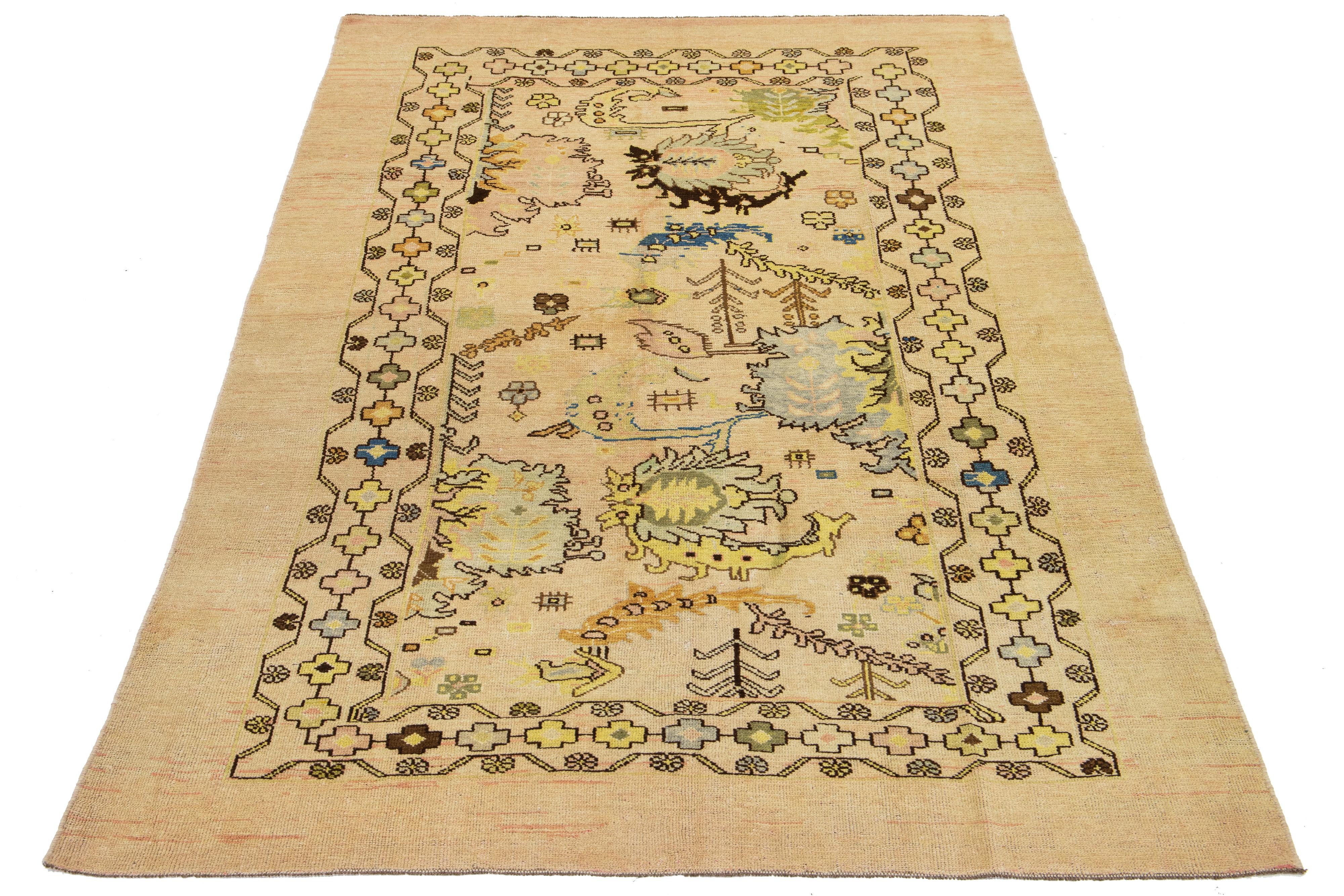Dieser schöne moderne handgeknüpfte Wollteppich aus der Apadana Revival Collection'S hat einen beigen Hintergrund. Es zeichnet sich durch ein auffälliges geometrisches und botanisches Blumendesign aus, das mit Blau-, Braun- und Gelbtönen akzentuiert