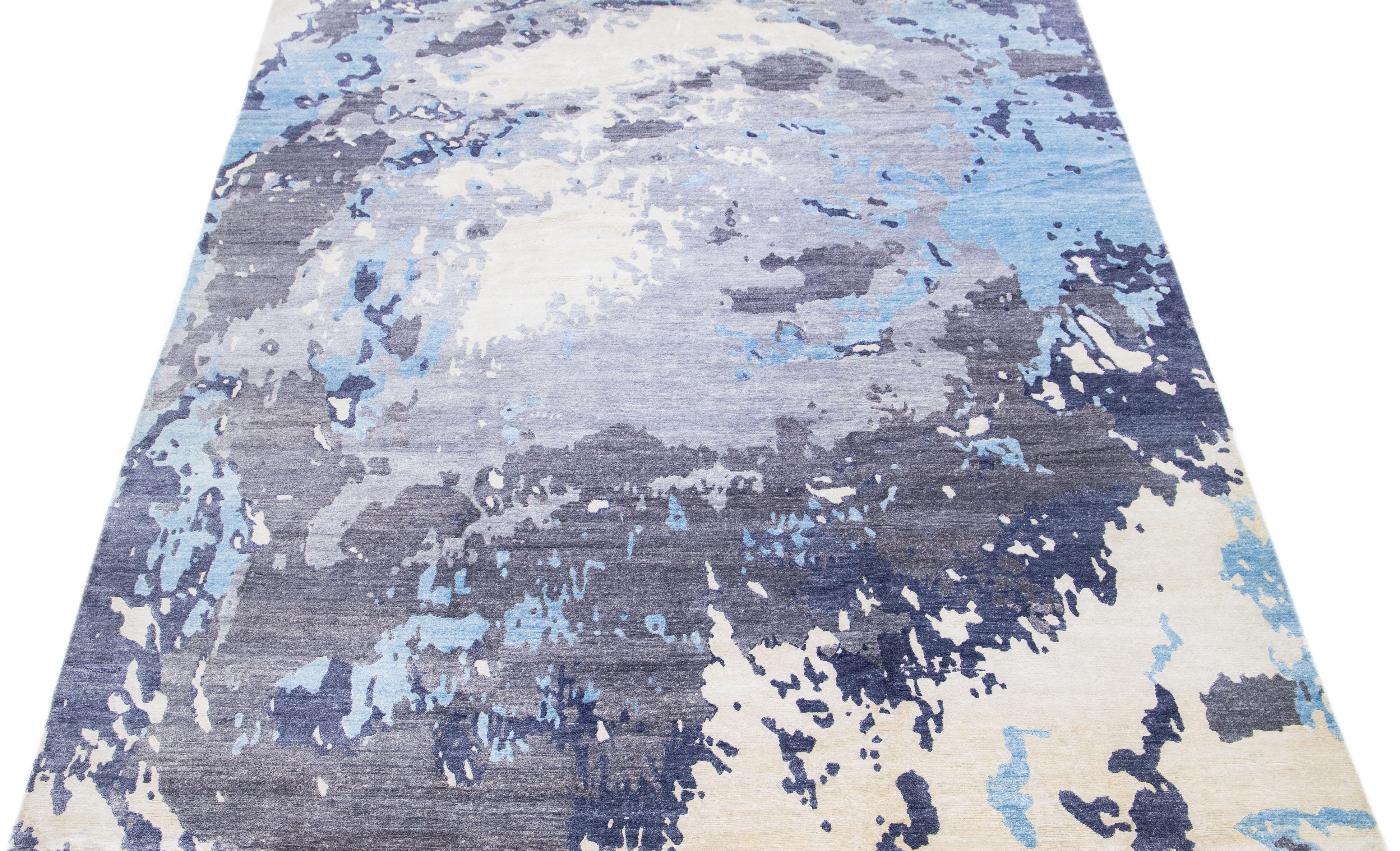 Dieser indische Teppich aus einer Mischung aus Wolle und Seide zeigt ein graues Feld mit einem abstrakten Muster in Blau und Weiß. Seine komponierten Materialien sorgen für Robustheit und Langlebigkeit, während sein ornamentales Design jeden Raum