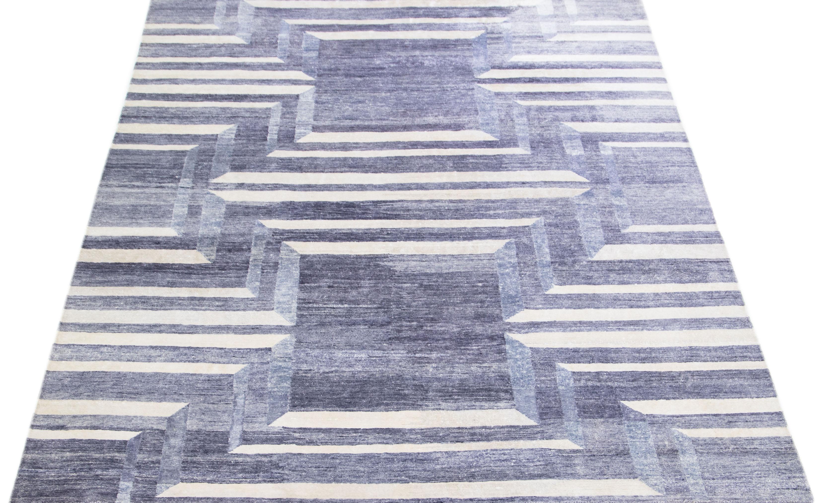 This wool and silk rug boasts a striking contemporary design featuring a captivating geometric motif in an elegant grey hue. The exquisite ivory accents perfectly complement the distinct abstract pattern, lending an alluring touch of glamour that