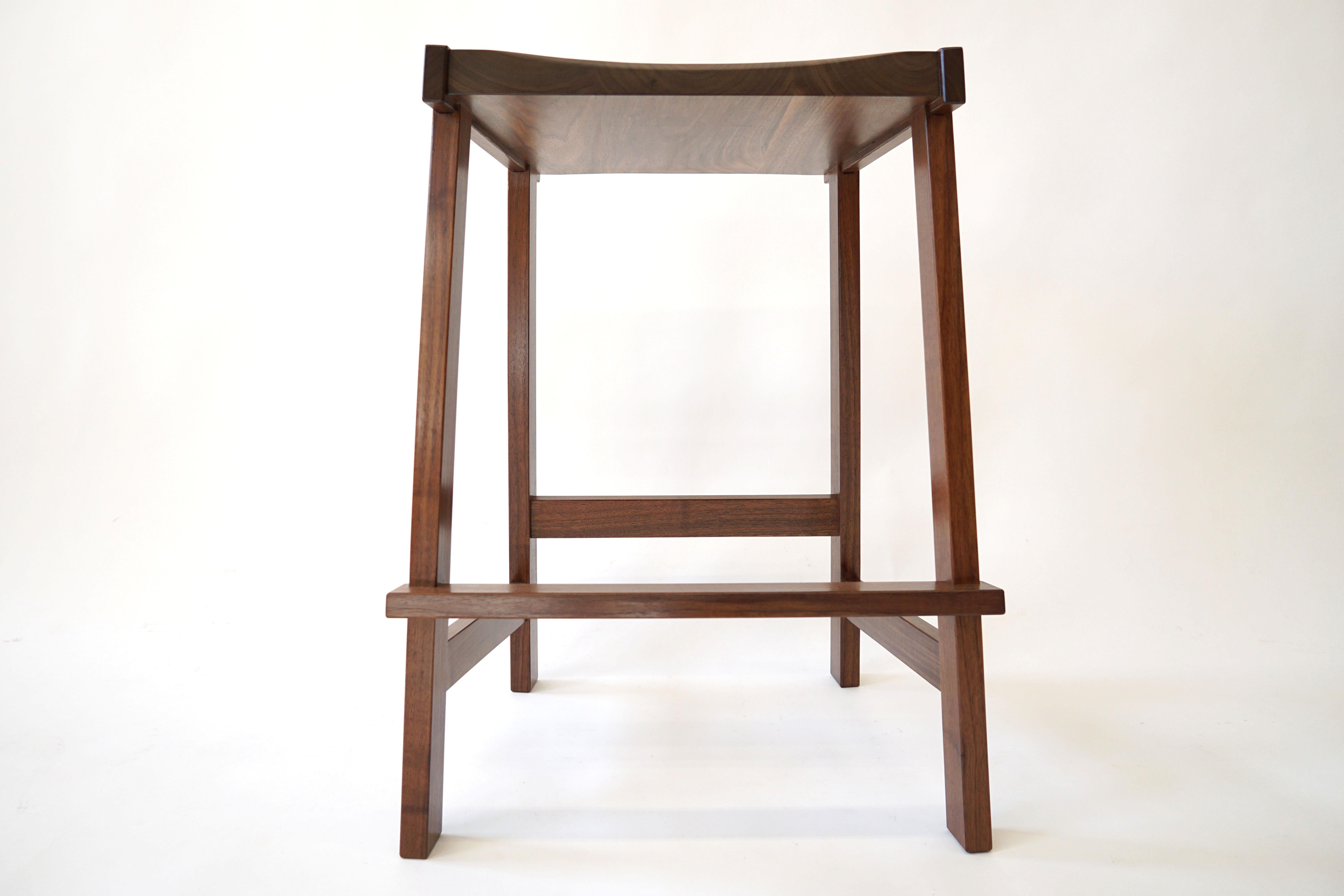 The Montrose Stool, a sharp, bold, angular form. Made from solid hardwoods with a carved seat for comfort. Constructed with lots of exposed joinery and interesting details. The top of the legs are bridle joints, let into the seat. The foot rest is
