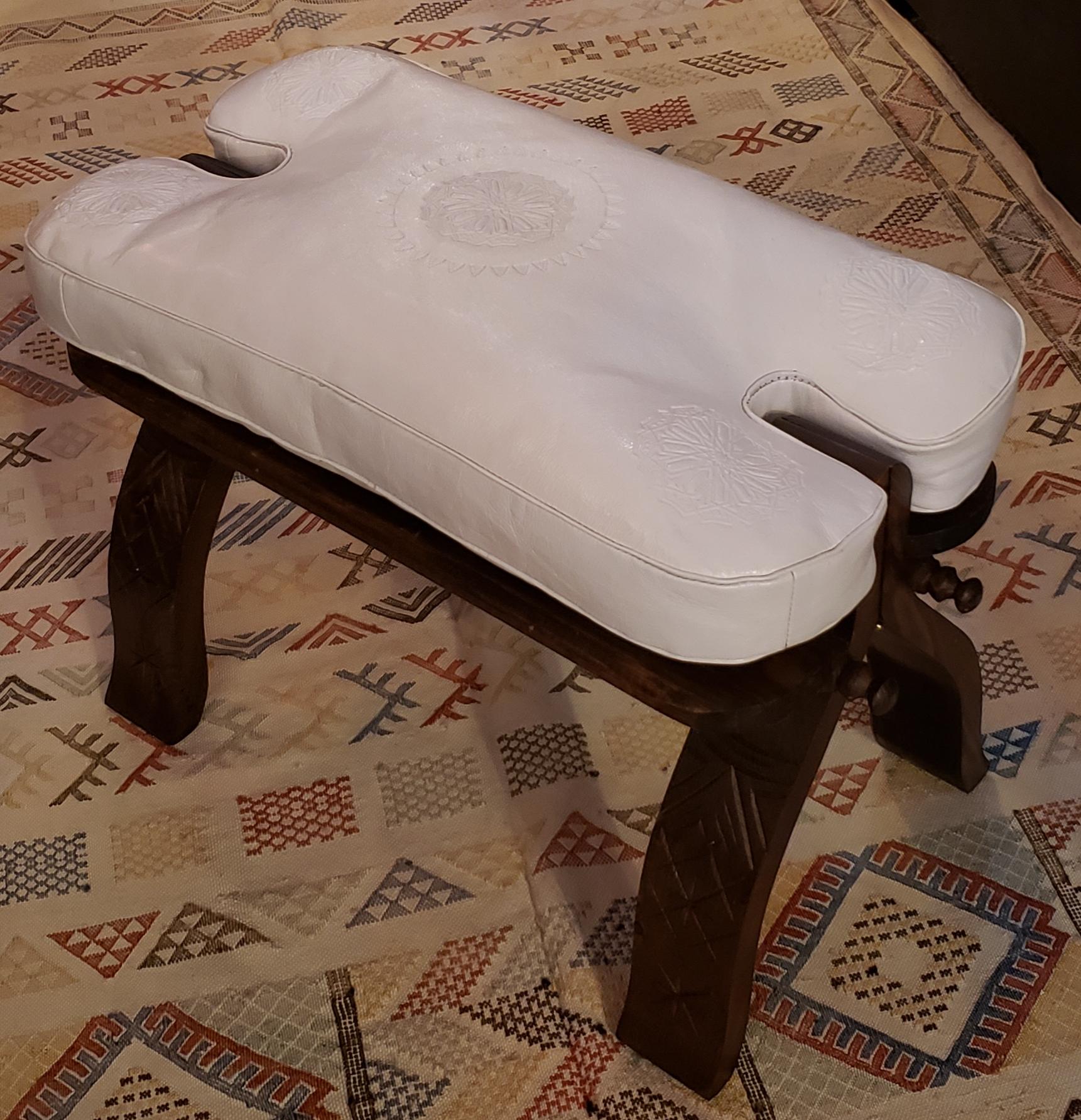 This is a great alternative to poufs and ottomans.
Handmade Moroccan camel saddle with genuine leather cushion and carved cedar wood base, measuring approximately 25 inches long, 13