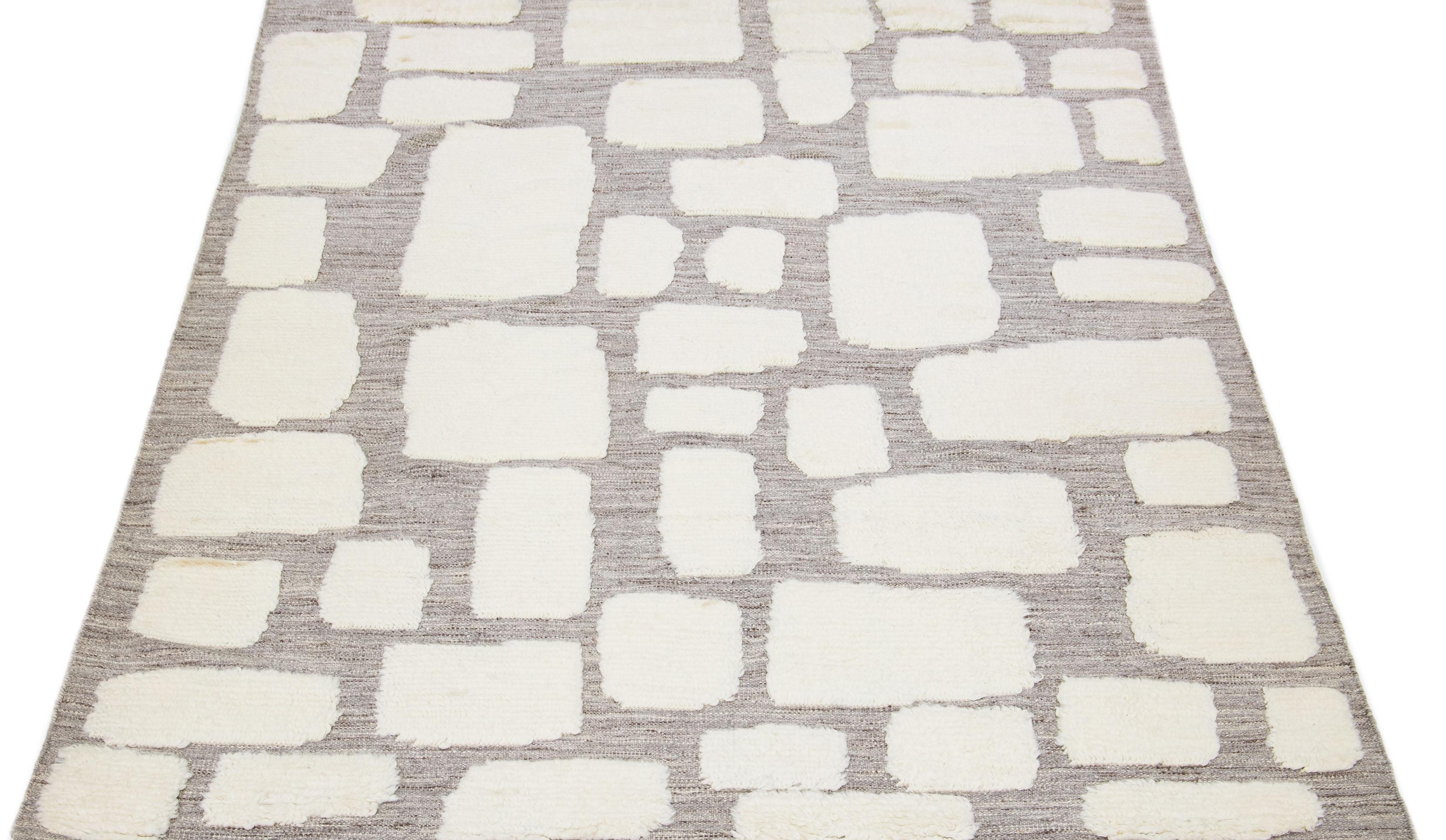 This hand-knotted wool rug showcases a contemporary Moroccan pattern in calm ivory shades, artfully set against a captivating gray background. The juxtaposition of colors creates a visually compelling abstract presentation that will leave a lasting