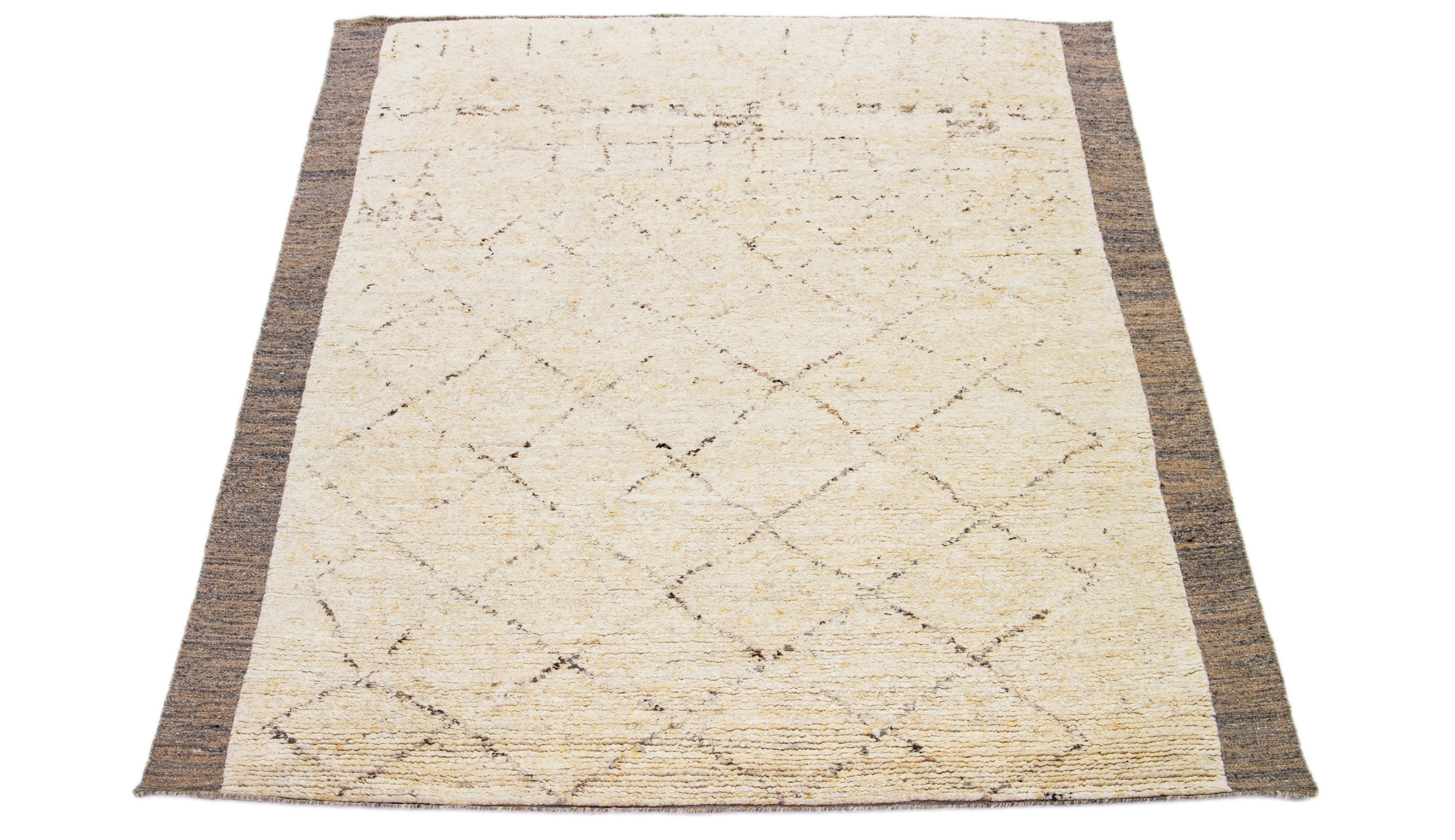 This exquisite hand-knotted wool rug showcases an elegant Moroccan pattern, predominantly in shades of brown and gray, surrounded by a refined frame and complemented by a captivating beige background. Its visually stunning Tribal exhibition imbues