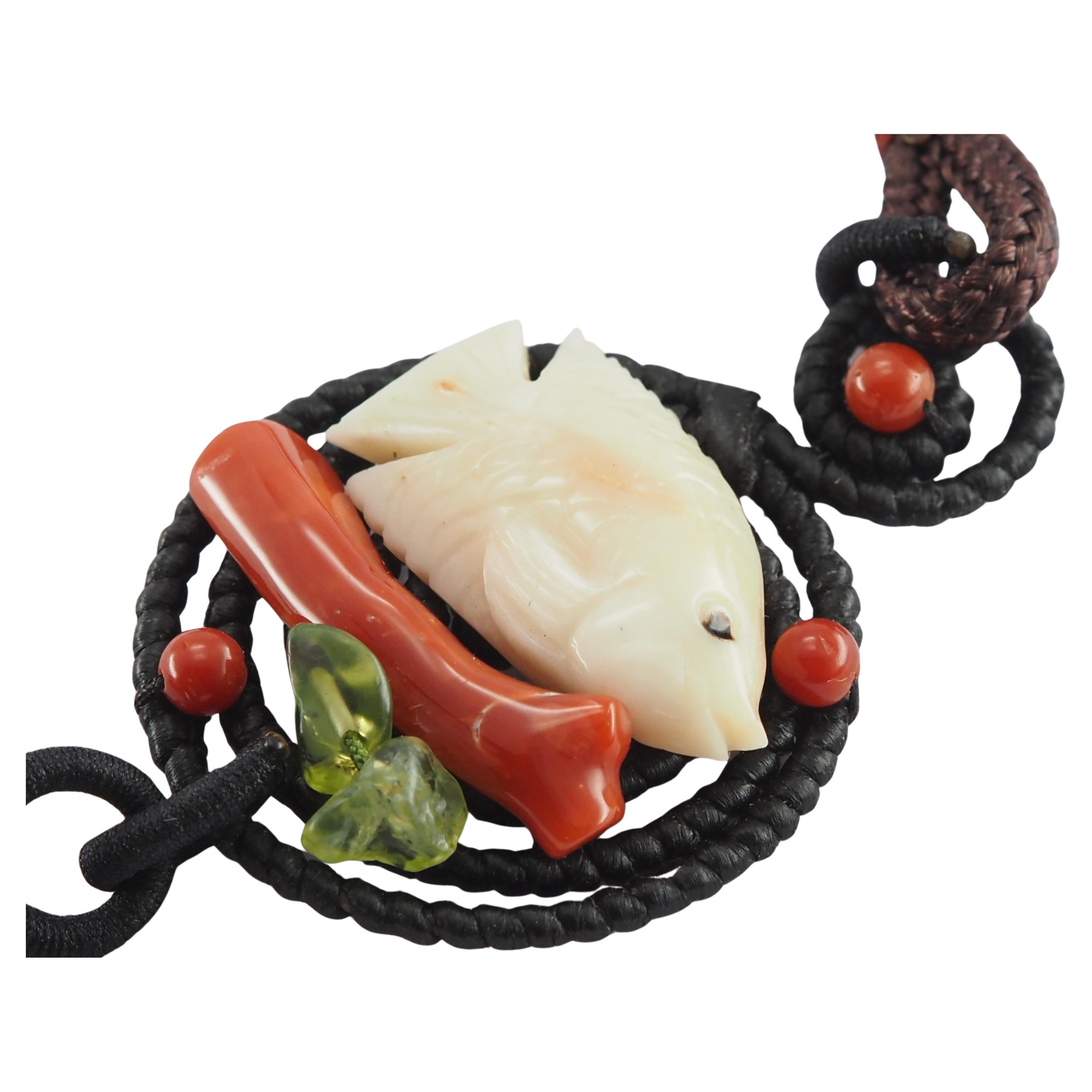 This handmade necklace features a beautifully carved natural white coral fish—a symbol of harmony, peace, and smooth energy. Beneath the fish lies a natural red coral stick, accented by two natural peridot gemstones. A handcrafted agate tassel adds