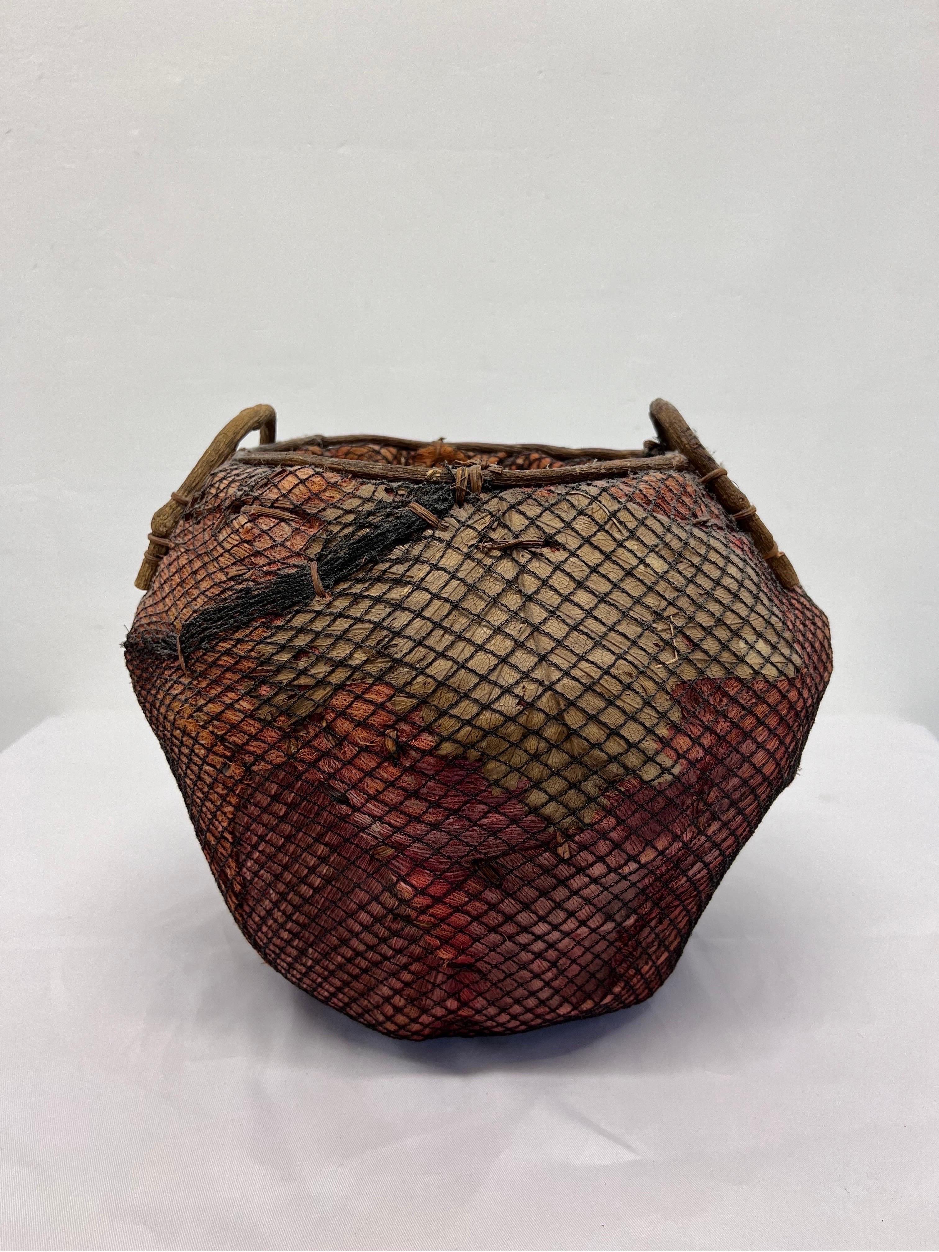 Woven natural fiber and leaf basket around a metal frame and wrapped in fishnet circa 1970s and made in the Philippines.
