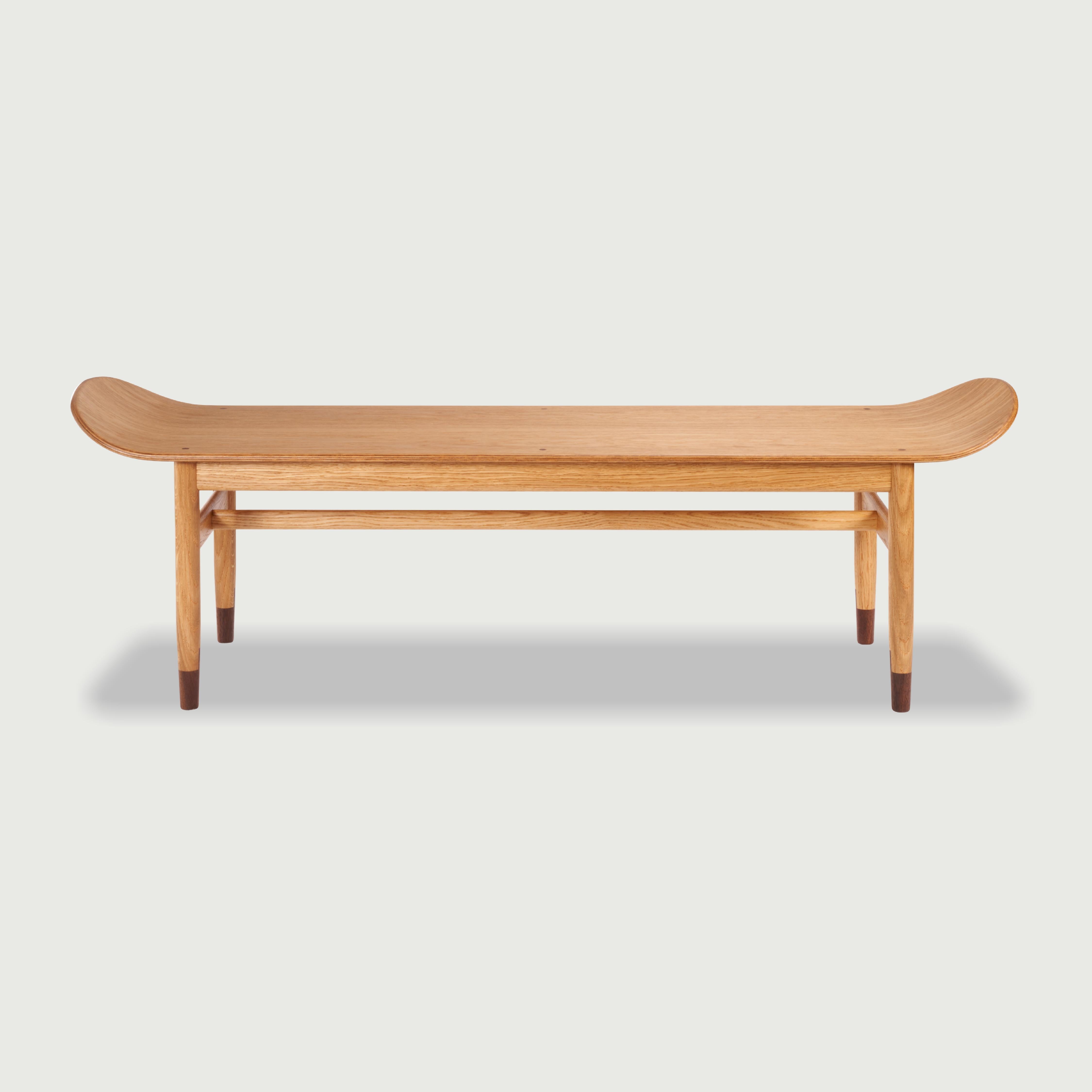 The bench made of oak with characteristic raised sides is hand cut and modelled. The seat built of 9 layers of 1.5 mm thick veneer creates a sturdy construction. Round tapered oak legs terminated with American walnut inserts are connected by