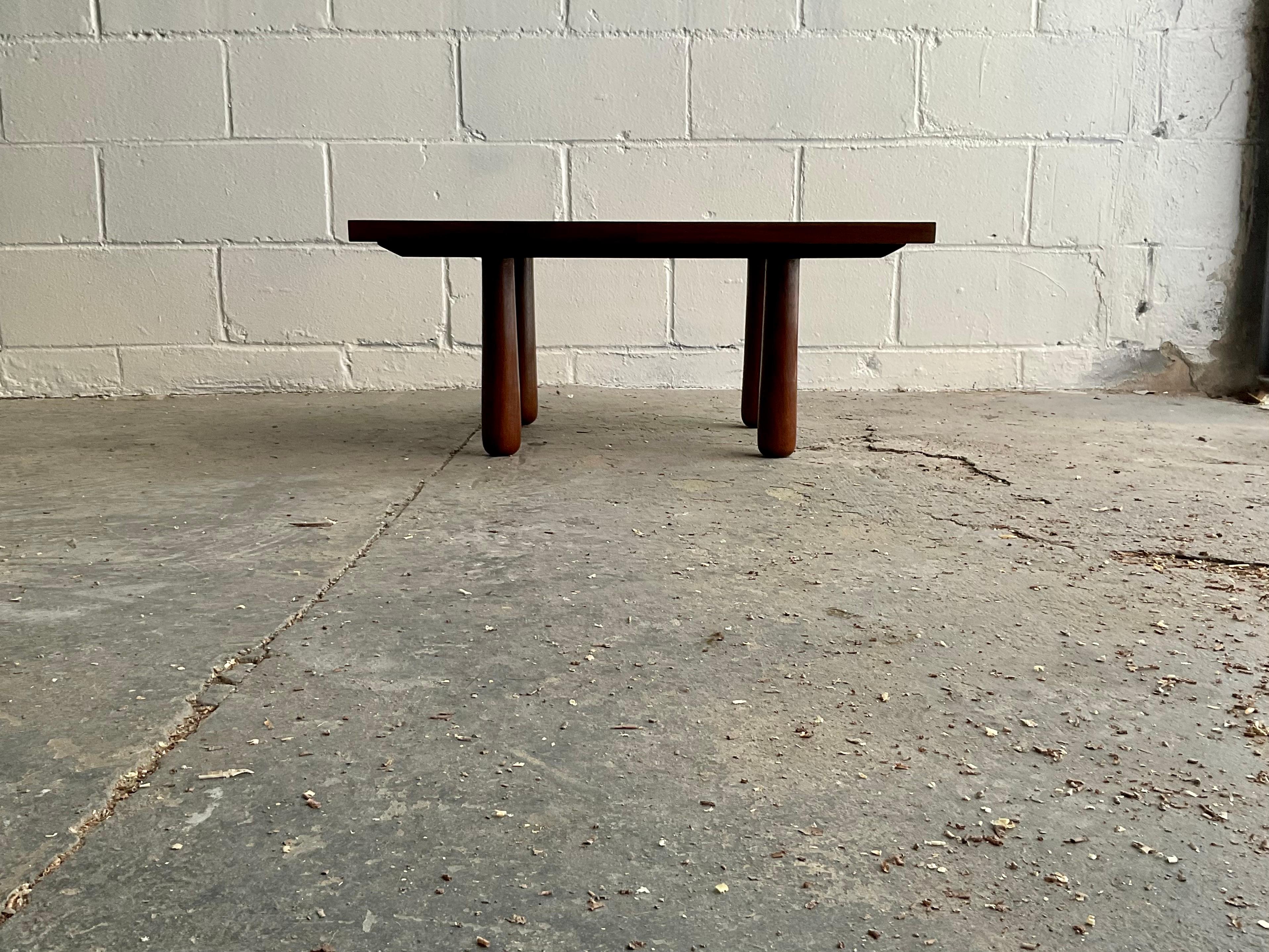 A lovely handmade low table in turned and laminated American Black Walnut, featuring visible joinery, tapered and rounded turned columnar legs, and a rail and stile panel with sapwood figure and live edge inclusion. This piece was designed and