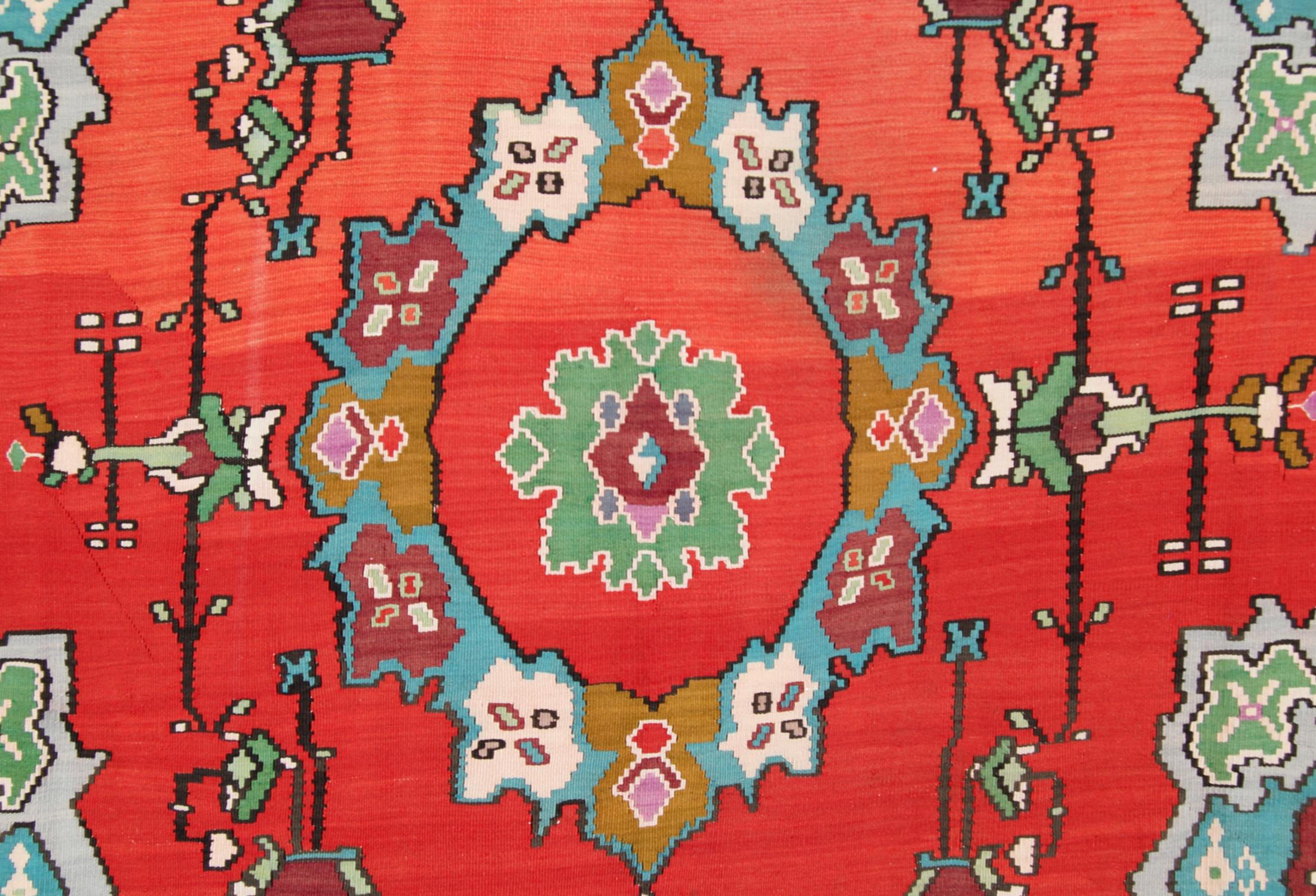 This blush red wool kilim rug was hand-woven in Turkey in the 1950s with an elegant medallion design. It featured three medallions woven in blue, mustard and pink accent colours on a red field with a symmetrical floral motif surrounding the pattern.