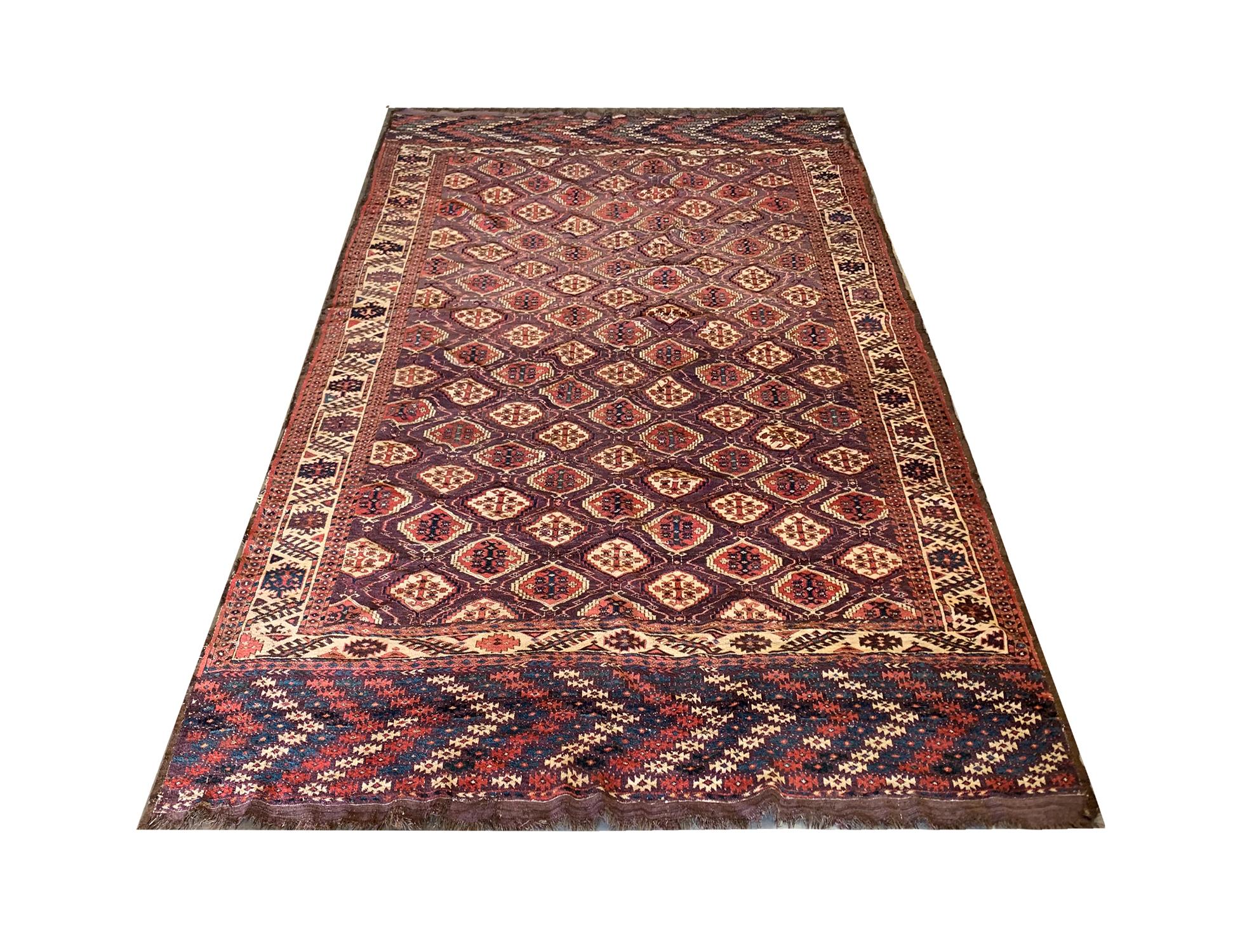 This antique wool carpet was woven by hand in Afghanistan in the 1890s by Turkmen people. The central design has been woven on a brown-red background with a repeating pattern geometric design made up of accents including cream and red. Sophisticated