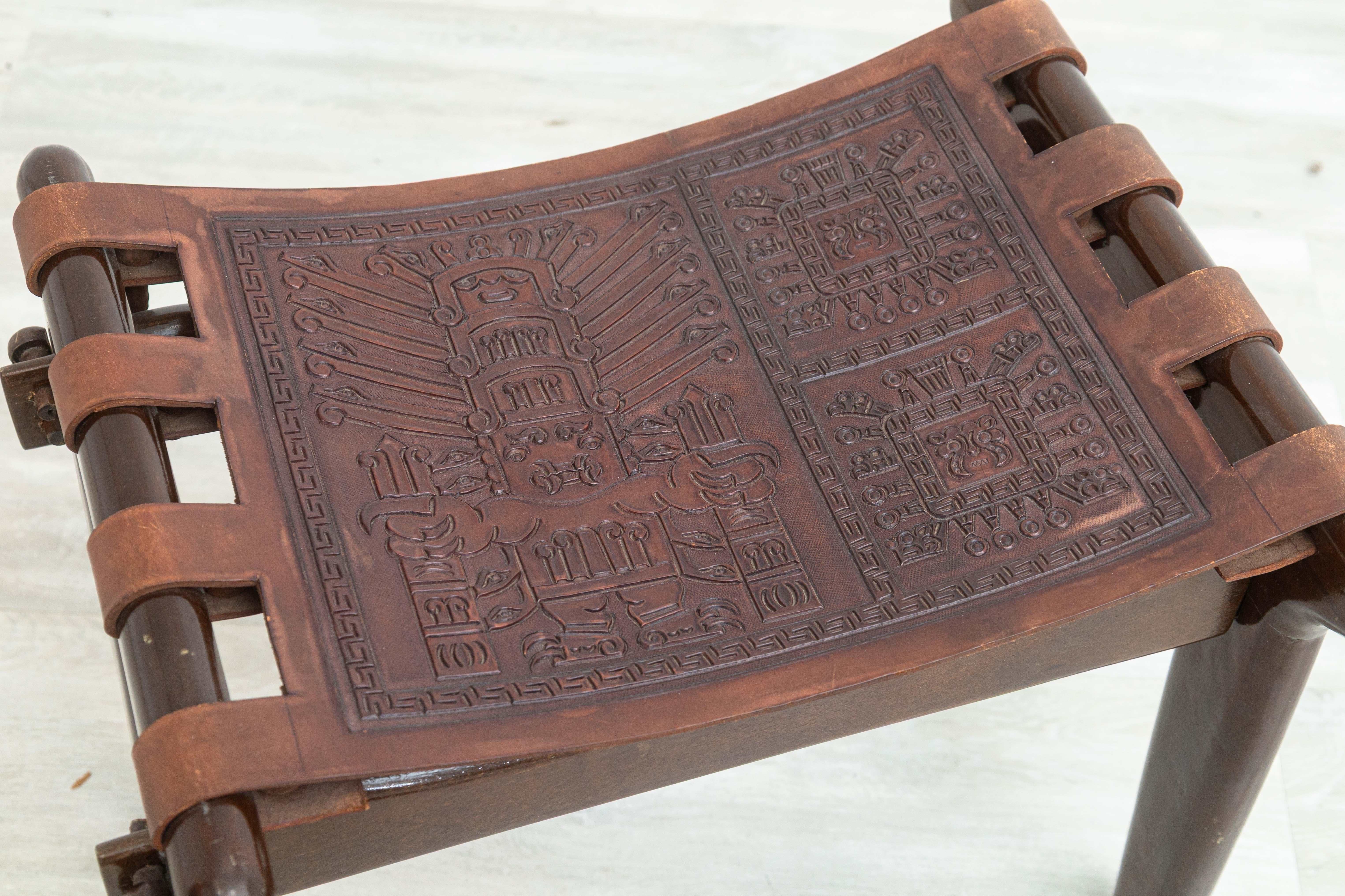 Uno sgabello di Angel I. Pazmino dall'Ecuador. Questo bellissimo sgabello fatto a mano presenta una seduta con cinghie di cuoio e incredibili disegni in rilievo. La struttura dello sgabello è arrotondata e intagliata a mano con una bella finitura
