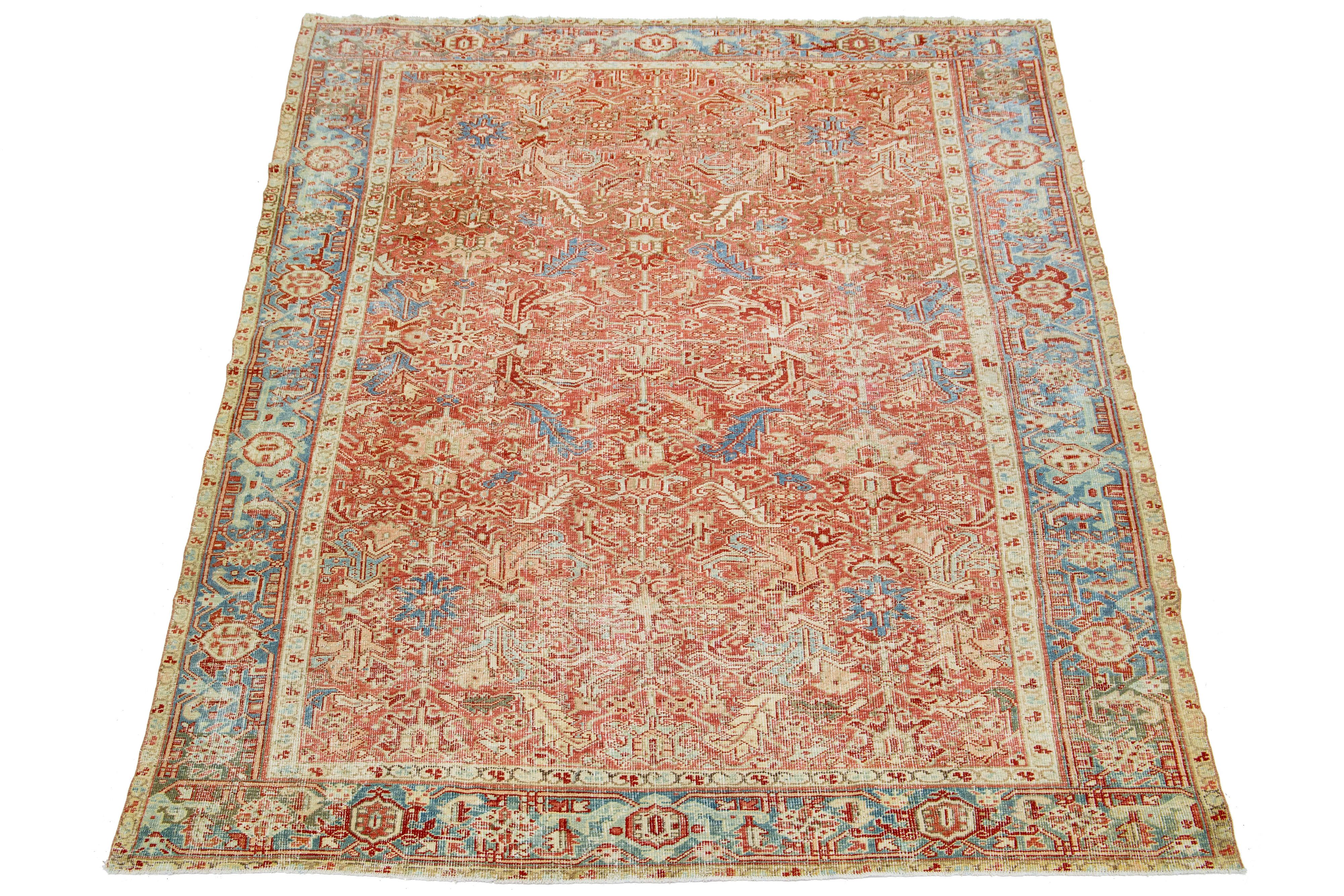 Der antike Heriz-Teppich besticht durch sein beeindruckendes Medaillonmuster und seine handgeknüpfte Wollkonstruktion. Das zart rostfarbene Feld bildet den Hintergrund für das auffällige geometrische Blumenmuster in Blau- und Beigetönen, das eine