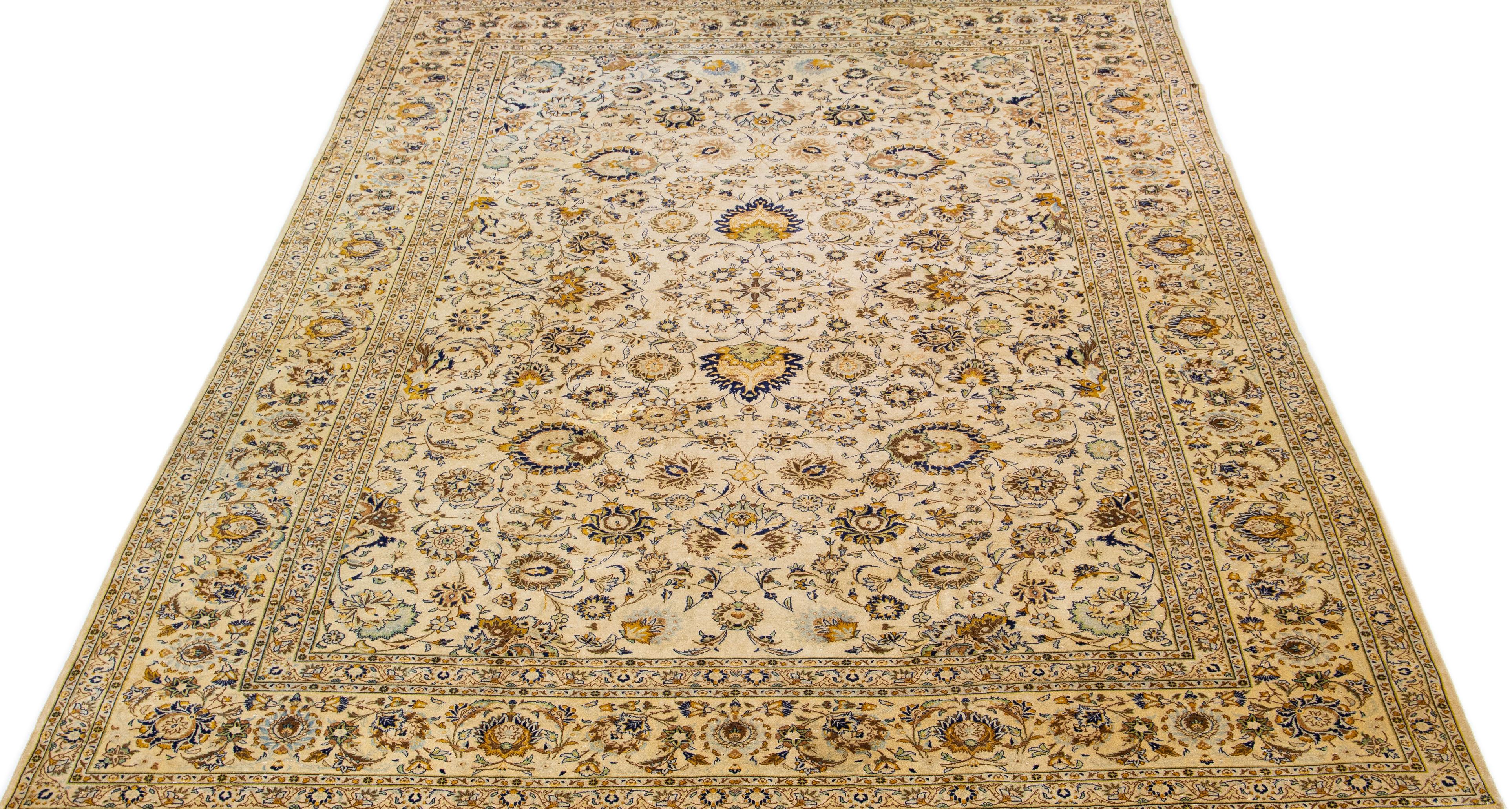 Beautiful antique Kashan hand knotted wool rug with a beige color field. This Persian rug has blue, yellow, and brown accents in a gorgeous Classic floral design. 

This rug measures 10'4