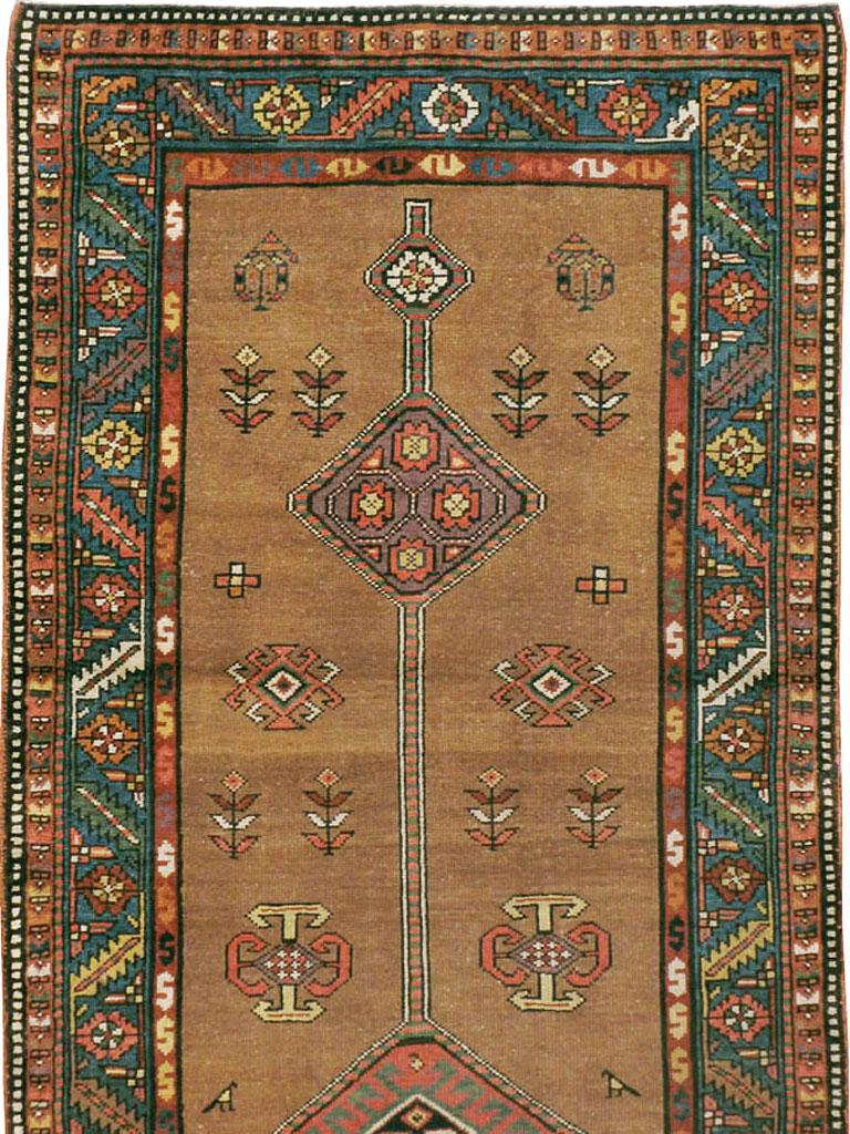 An antique Persian Serab rug in runner format from the early 20th century. The warm camel-tone brown field spaciously displays a long pole medallion punctuated by geometric lozenges, with stylized small flowers and rustic animals scattered about.