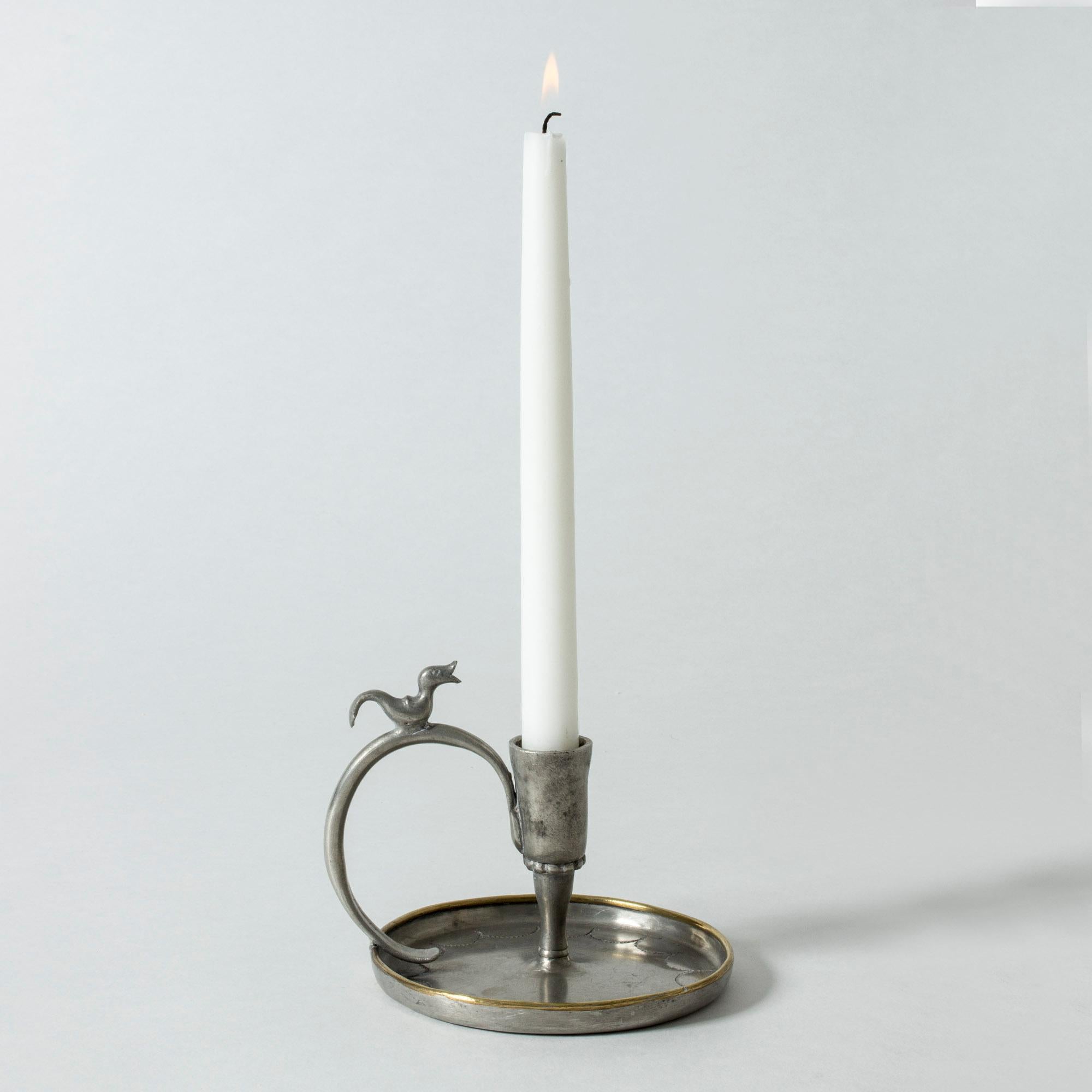 Handmade pewter candlestick by Nils Fougstedt, the original study for a candlestick that was later put into production by Svenskt Tenn. Decor of a duckling on the long arched handle. Punched pattern on the base, brass rim.

The candlestick