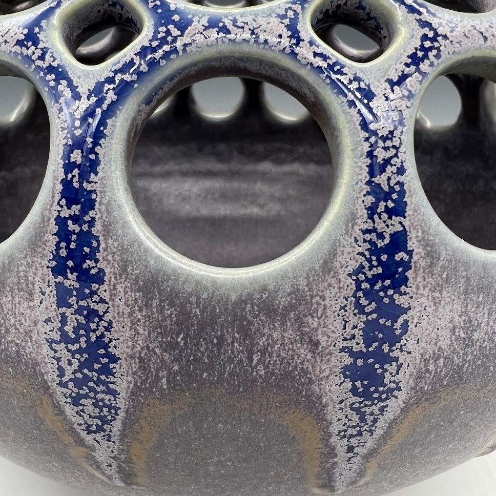 This piece is wheel thrown and hand pierced. When the piece is still wet, small holes are mapped out and pierced. Once the orb is bone dry, each hole is painstakingly enlarged. A single glaze is then sprayed on it in different thicknesses to create