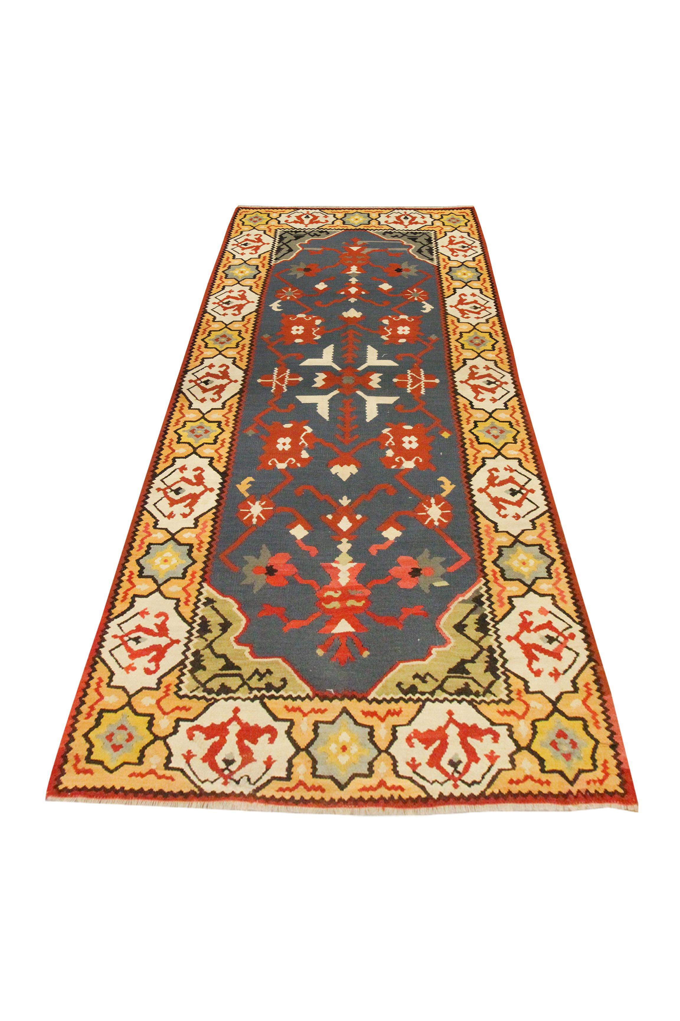 Red, blue, yellow and cream make up the main accent colours in this bold wool area rug. The central design has been woven on a blue background with red and cream accents that make up the symmetrical pattern. A yellow repeating pattern border has