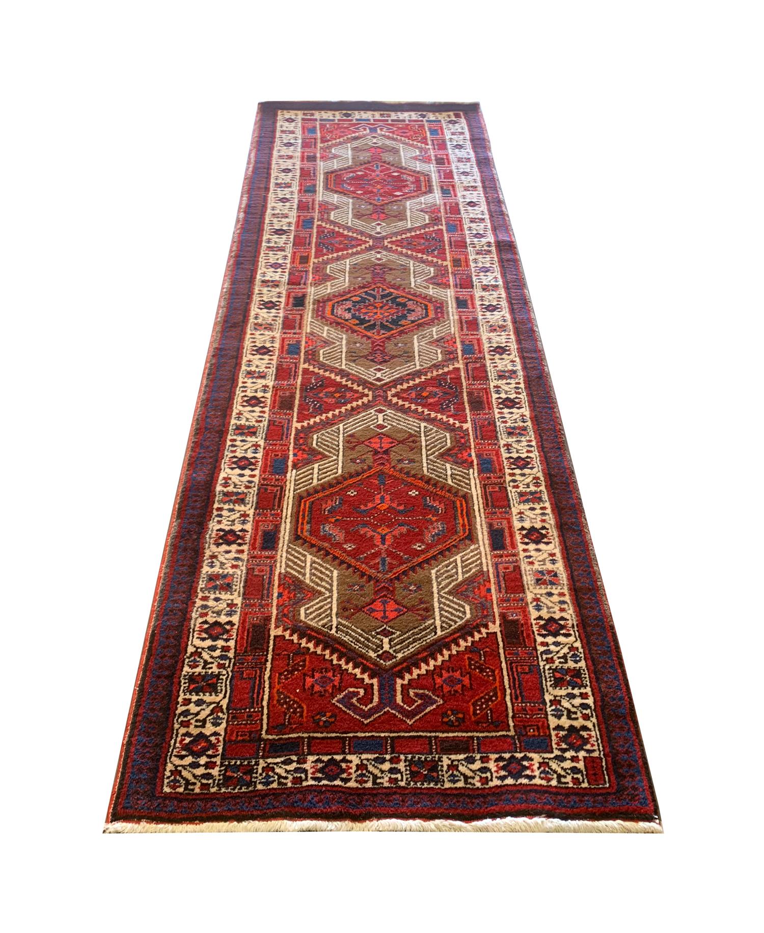 Questo audace tappeto in lana è un eccellente esempio di tappeto runner tessuto all'inizio del XX secolo, intorno al 1930. Il disegno centrale presenta un trio di medaglioni delicatamente intrecciati in rosso e blu con accenti beige e crema. Un