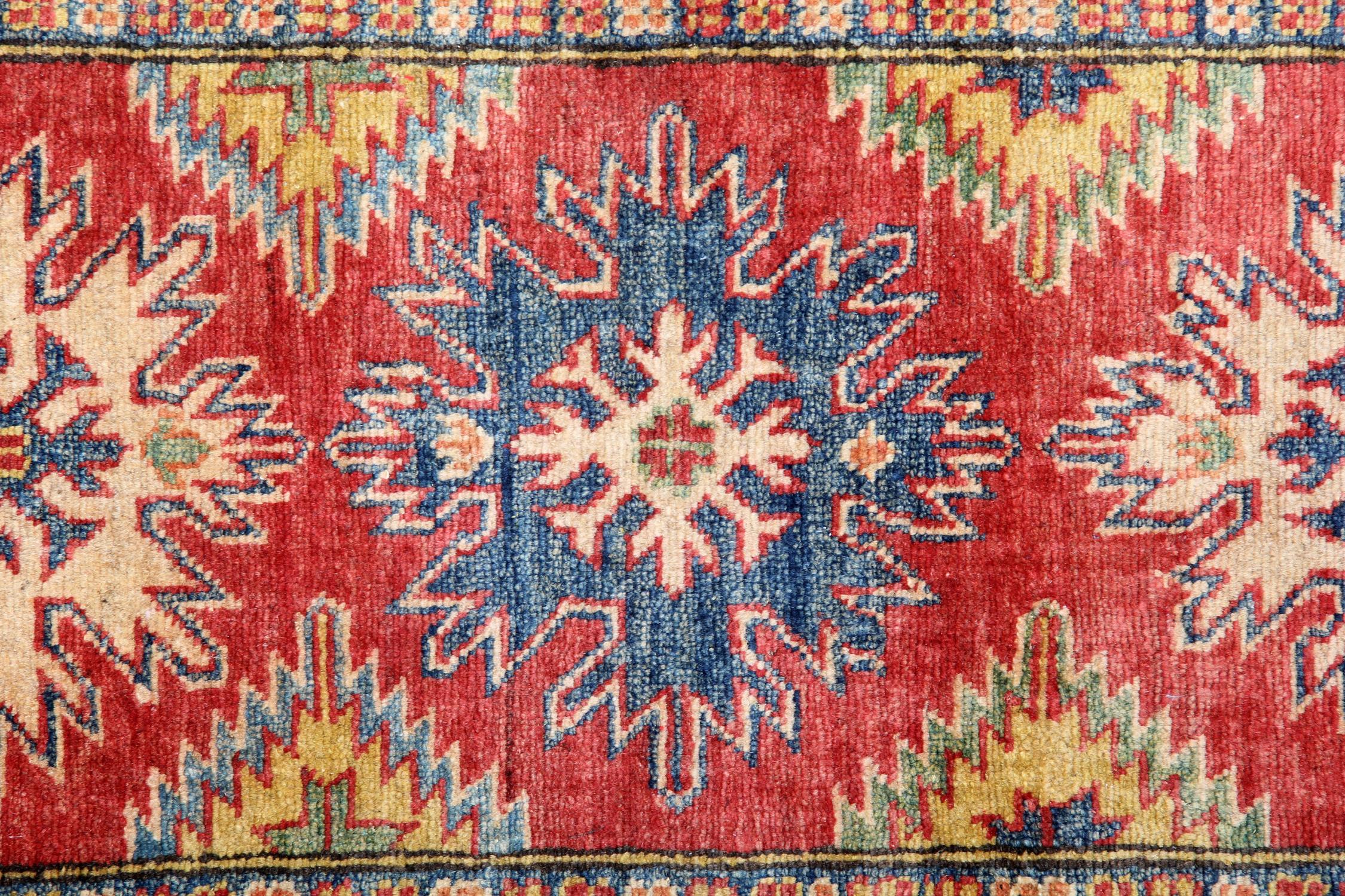 This handmade carpet runner's new traditional handwoven Kazak rug comes in a striking colour combination. This red rug has cream, red, blue and caramel accent colours woven through both the centre and border. The pattern depicted on this hand-woven