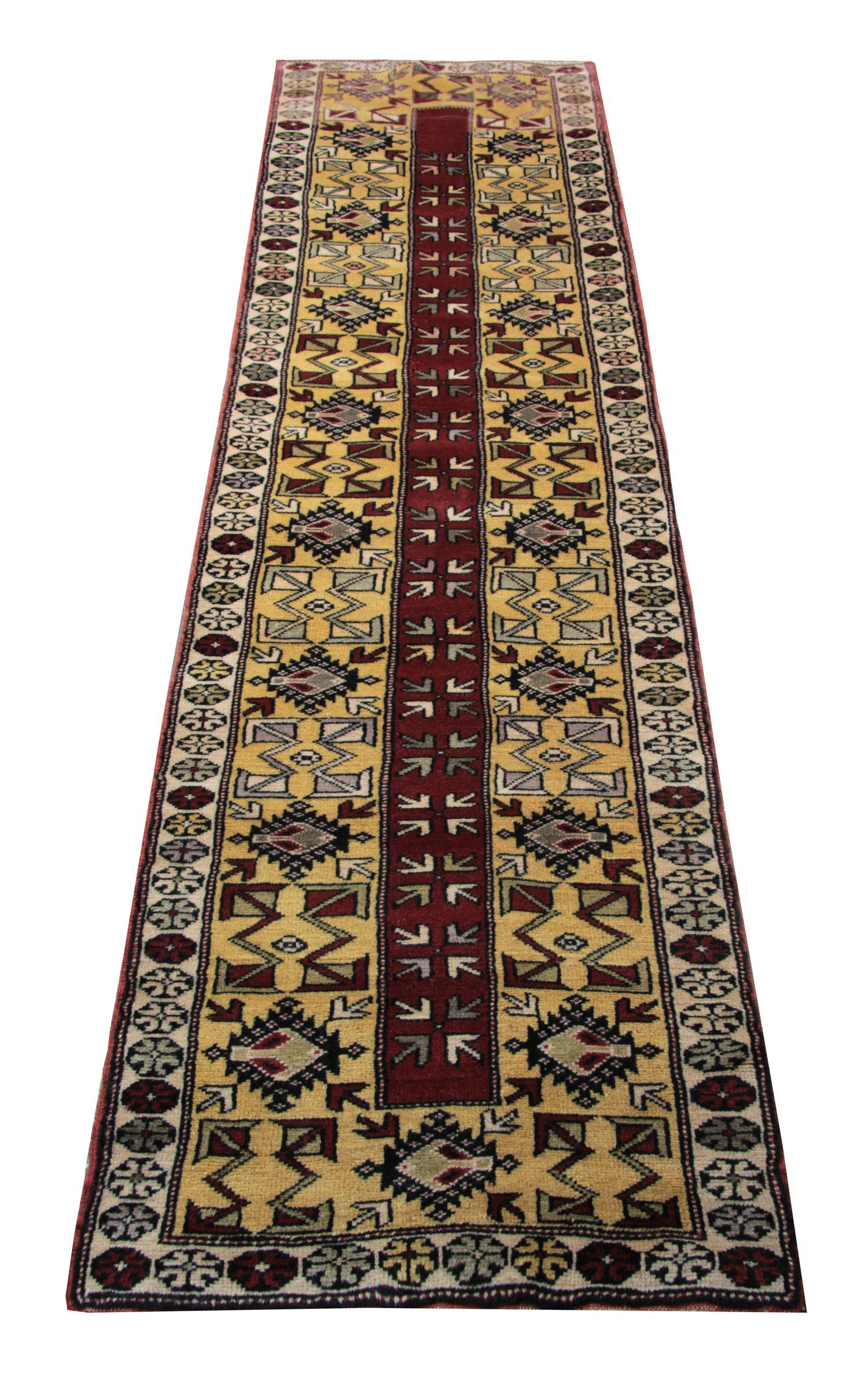 This fine wool runner rug was woven by hand and features a symmetrical geometric design. Featuring a beige-yellow background with red, brown, and blue accents that make up the elegant geometric repeat pattern design. This is then framed by a repeat