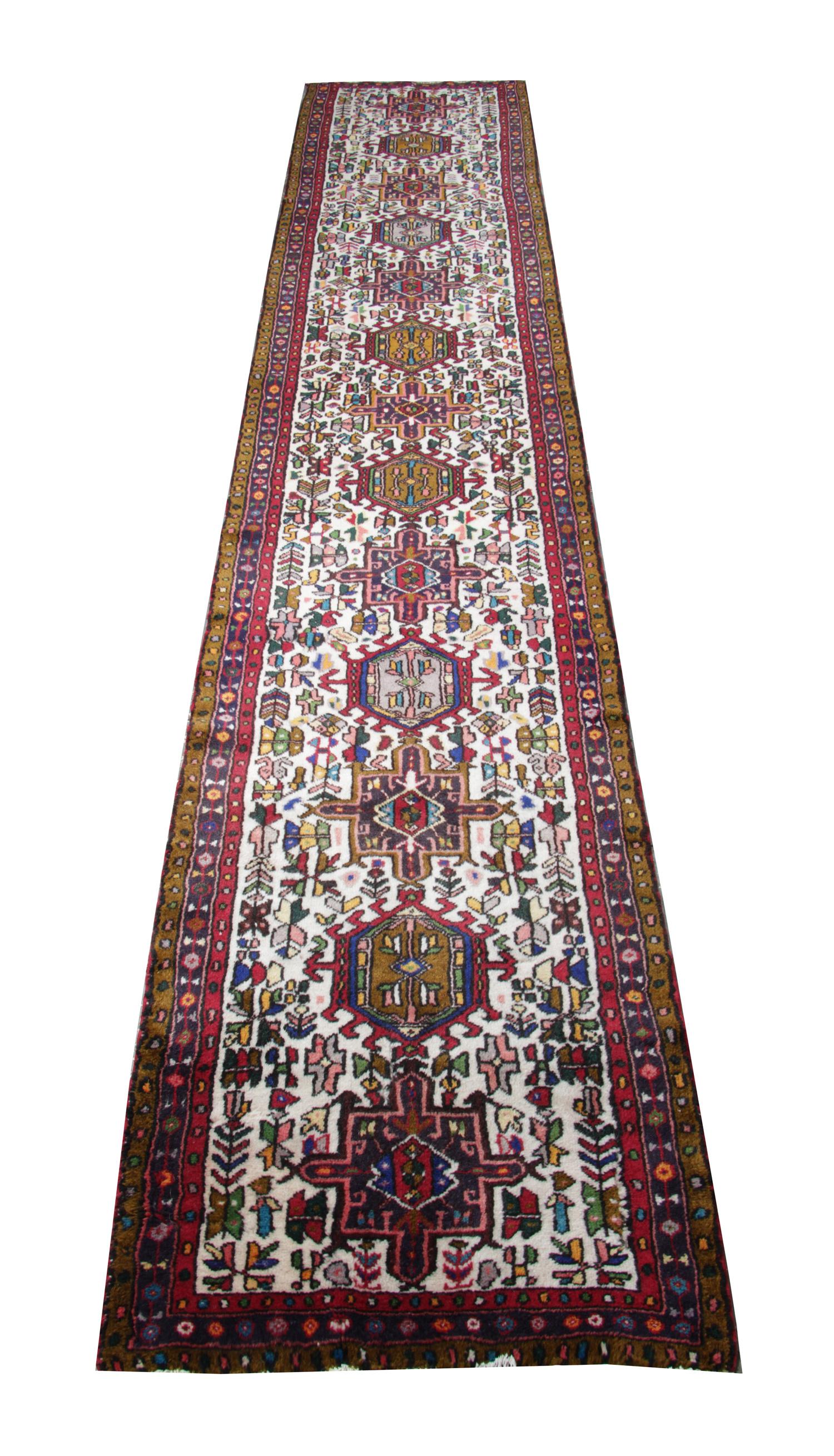 This elegant geometric runner rug was woven by hand in 1960. The central design has been woven on an ivory background with red, blue, yellow and pink accents that make up the medallion design. Intricately woven with small motifs in the surrounding