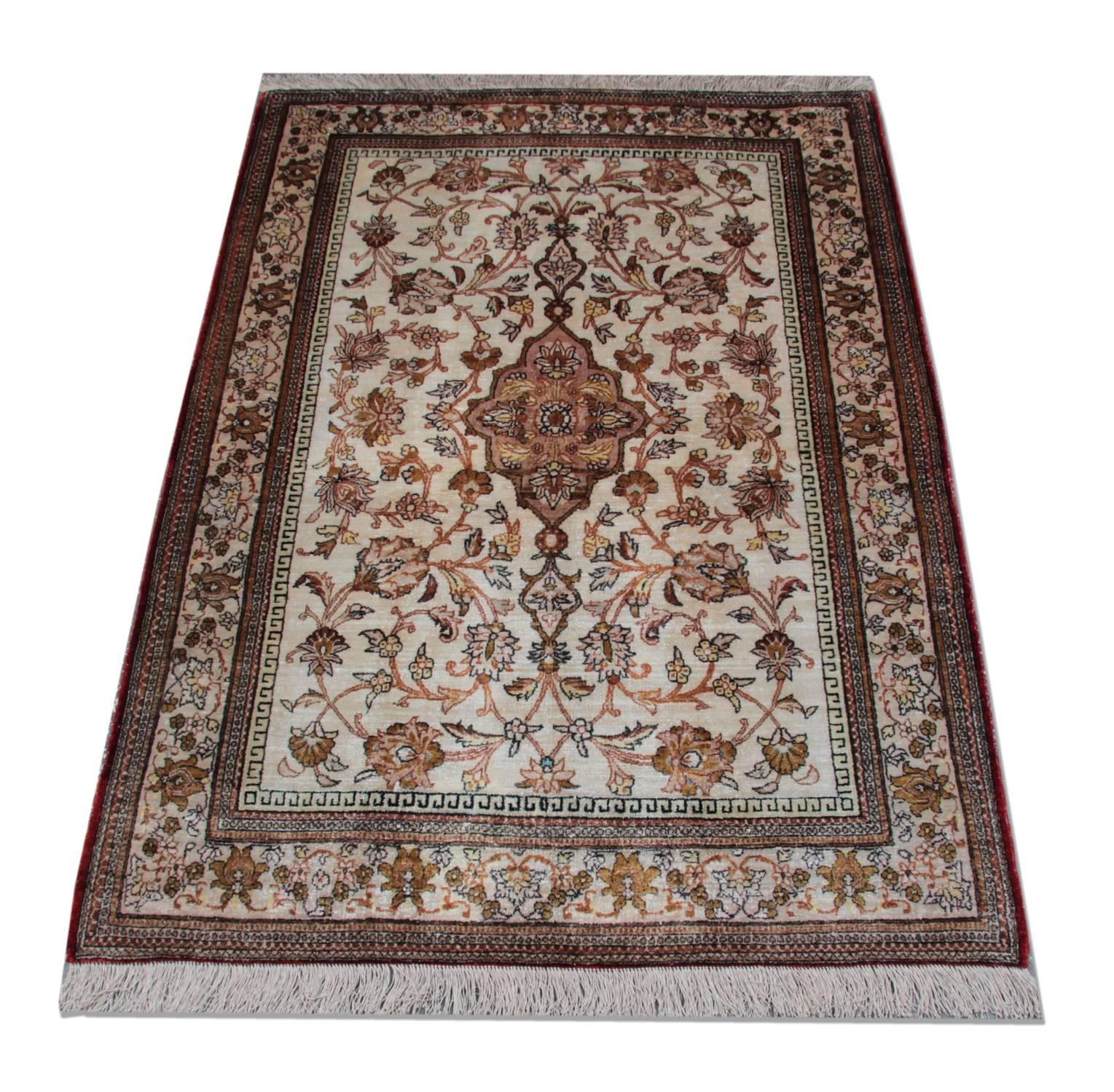 This fine silk area rug was woven by hand in Pakistan in 1960. The central design features a cream background that has been decorated with a central medallion and symmetrical surround design with wondering floral motifs, woven in beige, cream and
