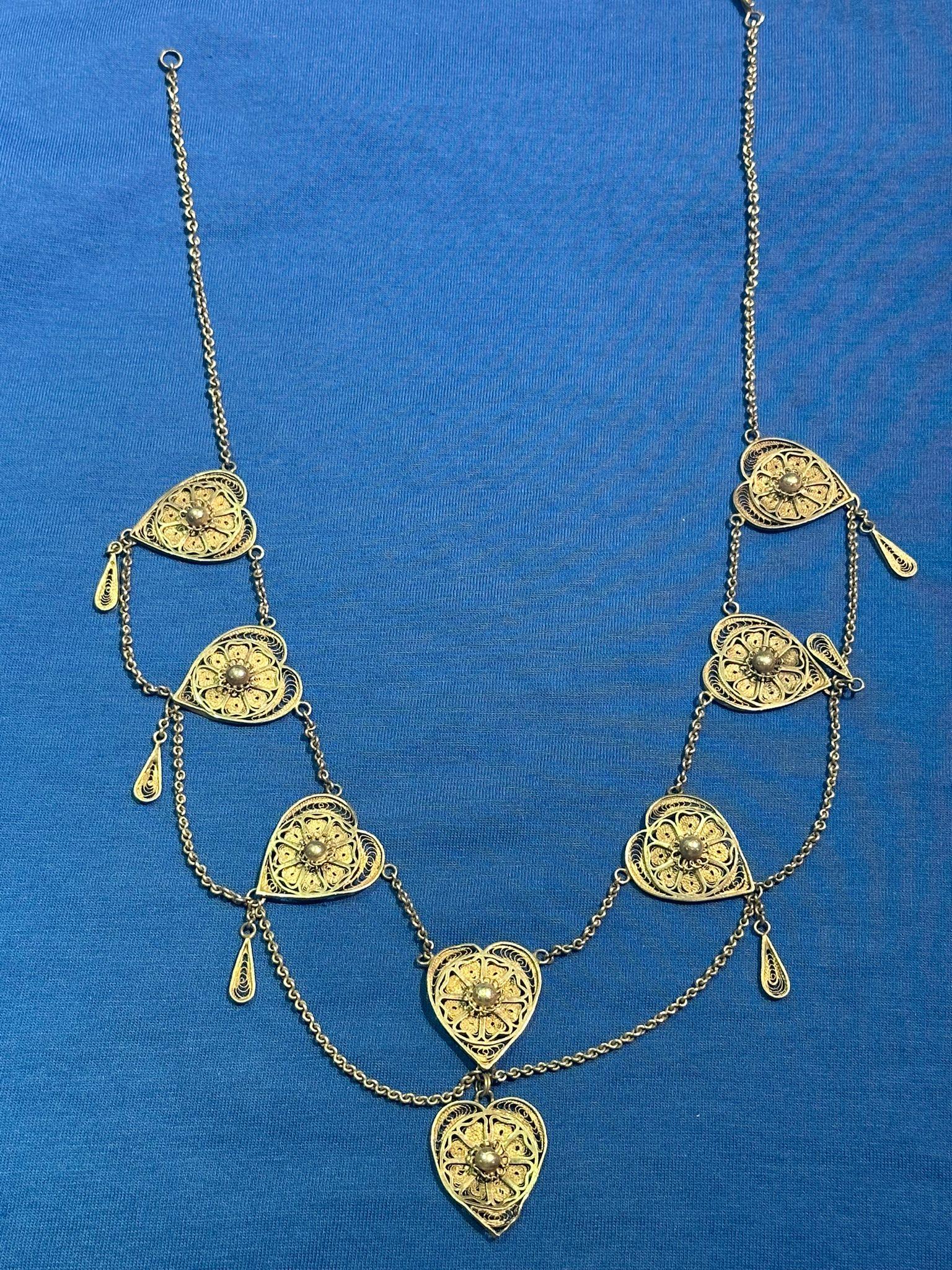 This exquisite handmade necklace, crafted around 1920 by artisans of the Bezalel School of Arts and Crafts in Jerusalem, is a masterwork of silver filigree jewelry. The necklace features a stunning symmetrical design composed of nine heart-shaped