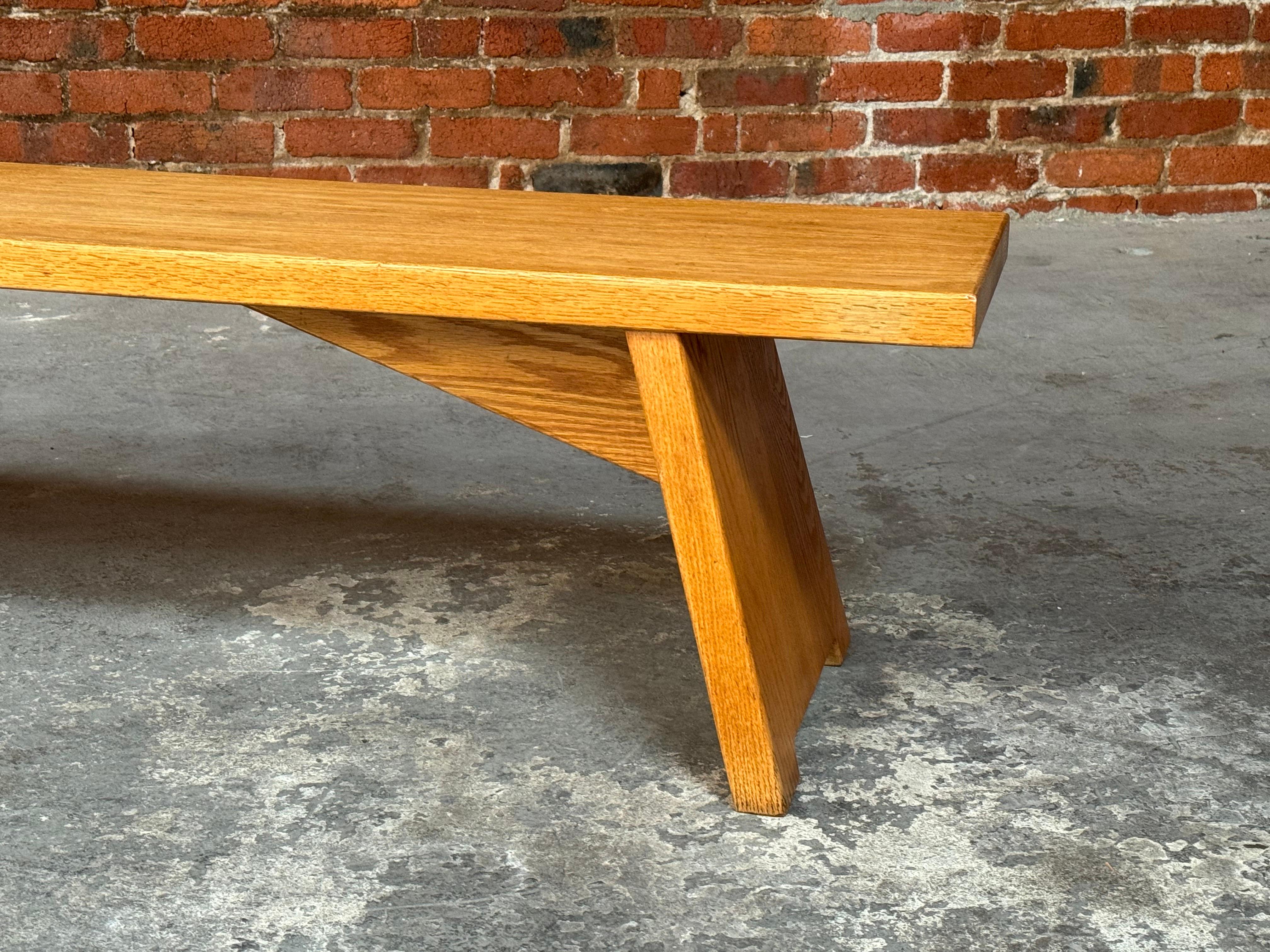 Handmade  solid oak bench in the style of Pierre Chapo, a slender profile with architectural details to the legs and strut supports on the underside. The bottom of the legs have slight cutout to create openness. The oak has turned into a nice honey