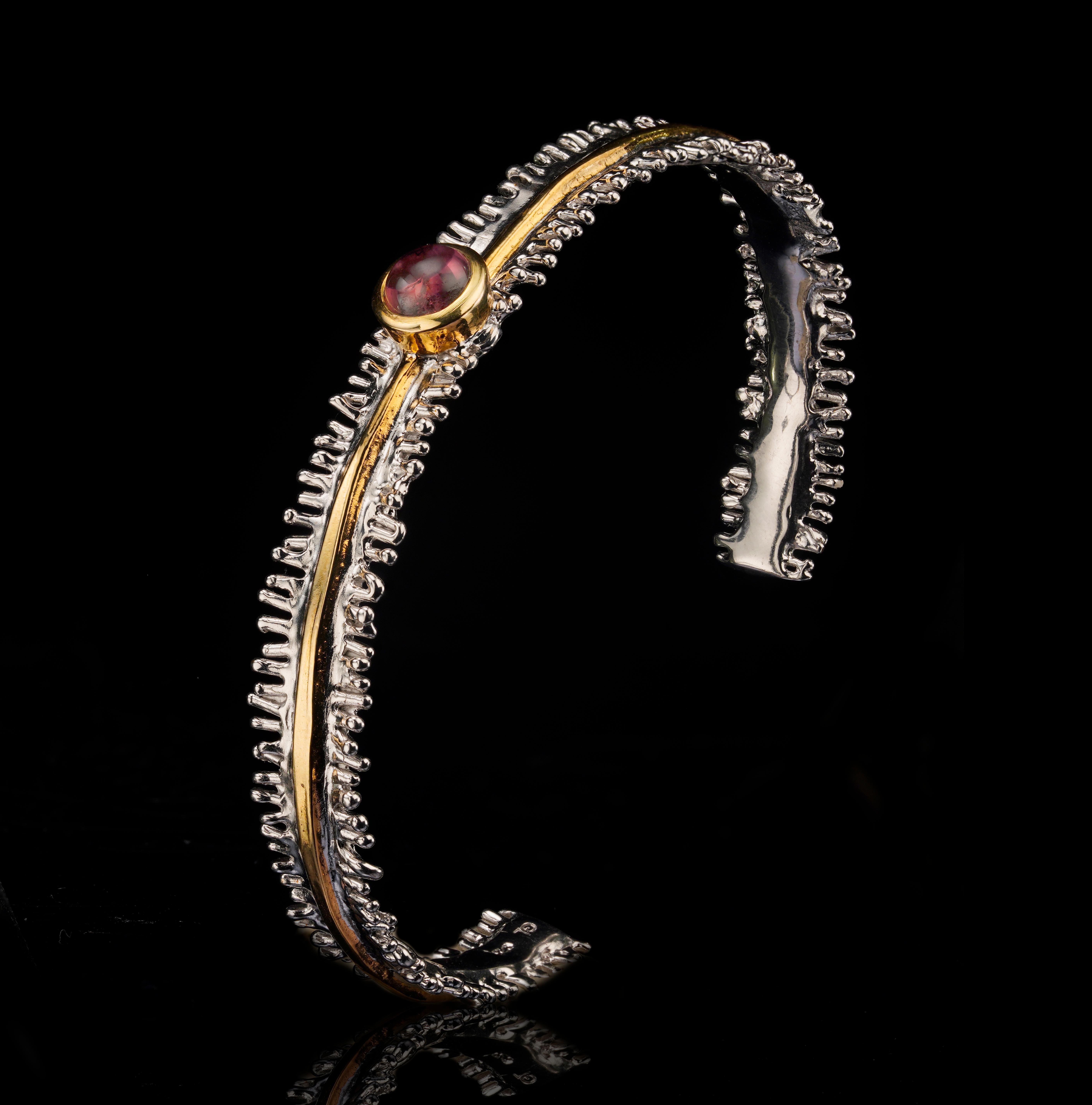 Eleva la tua collezione di gioielli con questo squisito bracciale d'argento fatto a mano con tormalina rosa e accenti d'oro e ornato da una vibrante tormalina rosa al centro. Questo straordinario bracciale fatto a mano presenta una luminosa gemma di