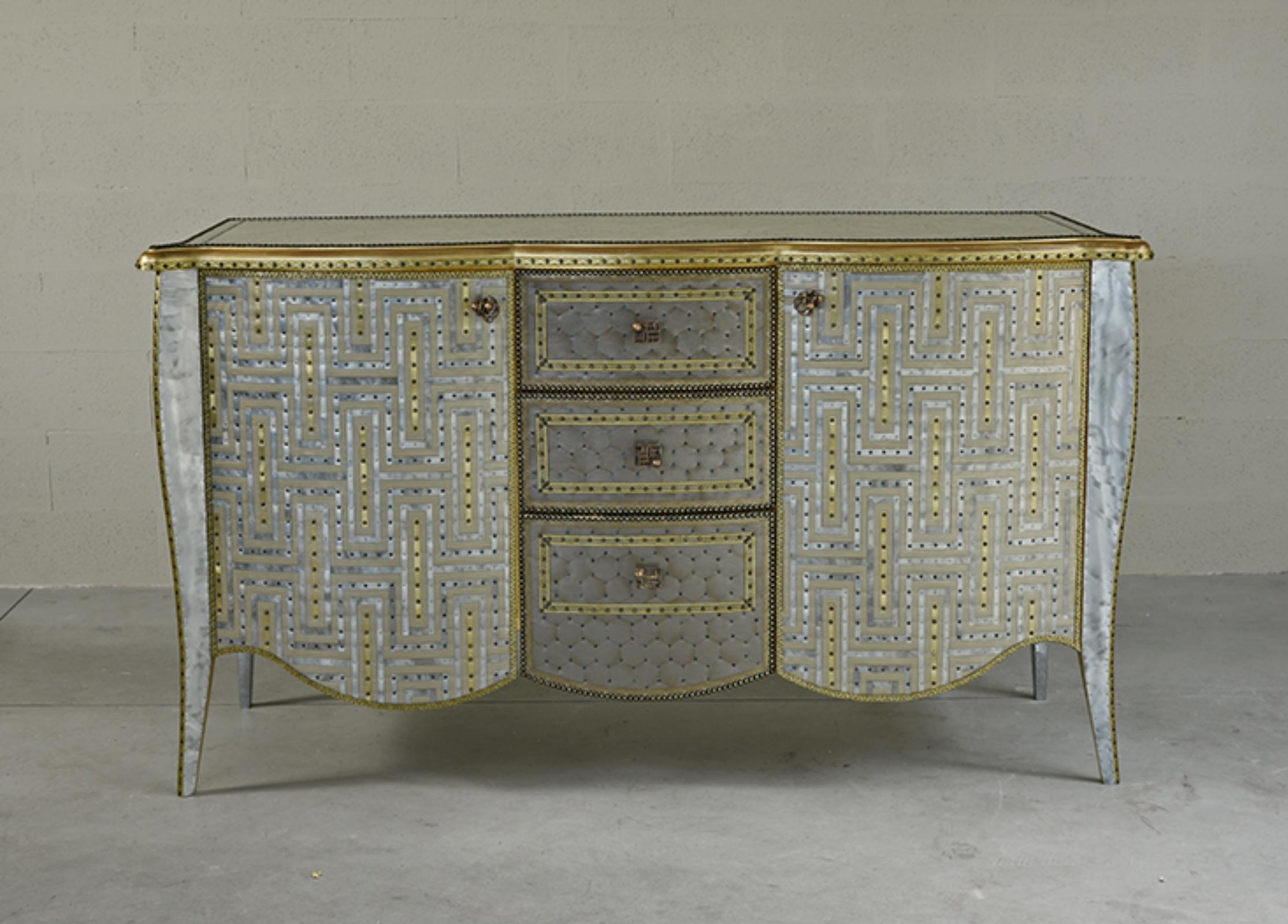 Buffet artigianale di lusso in 
Struttura in legno, tessuto, lamiere rivestite in ottone e zinco, strisce di ottone, fibra di vetro, chiodi, borchie
Realizzato a mano in Italia.
Dimensioni: 170cm x 65cm H. 95 cm

 
Pieno di splendore che si declina