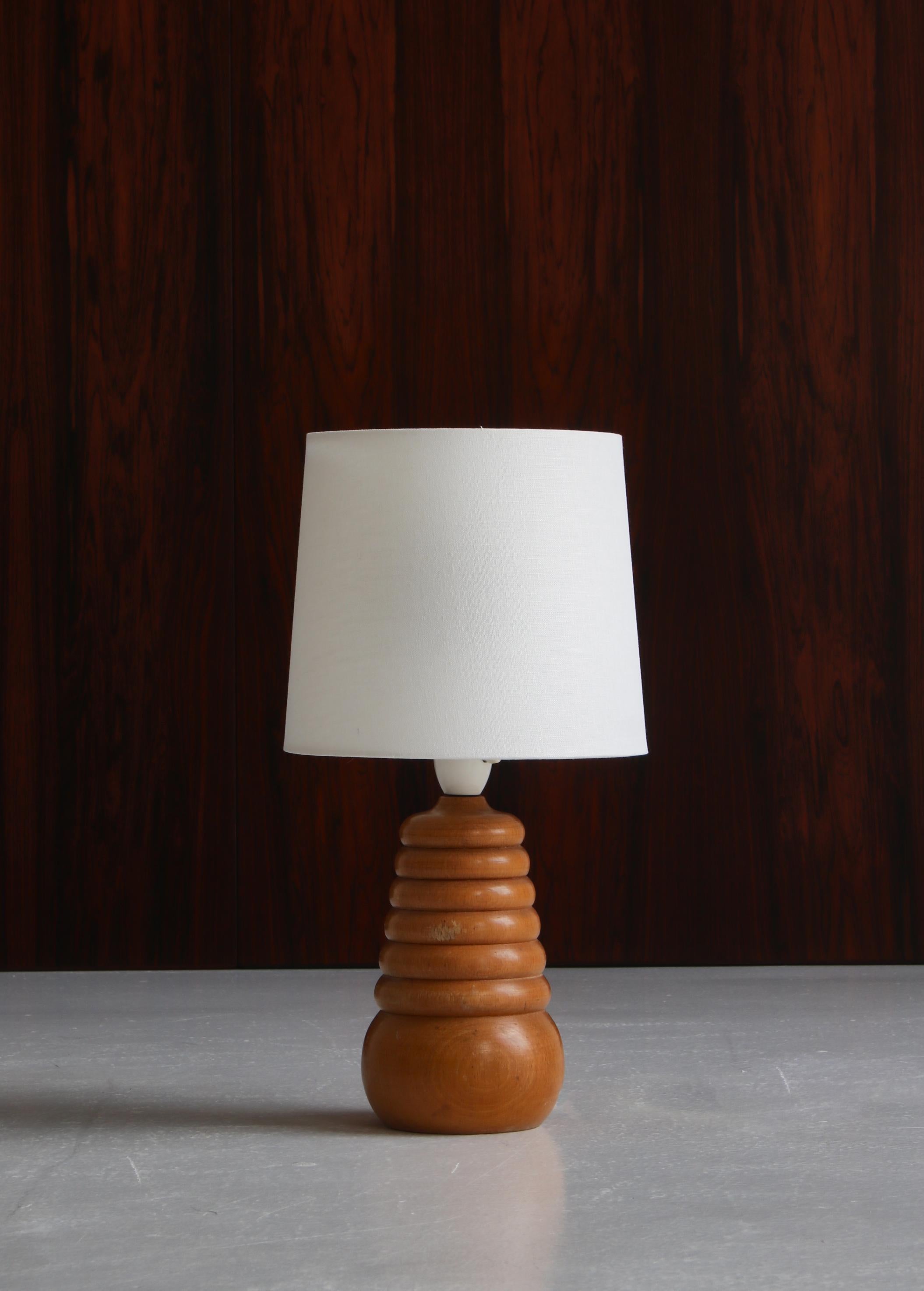 Charming unique table lamp in turned beechwood by a Danish cabinetmaker. Made in the 1950s Denmark. Equipped with white flax linen shade.