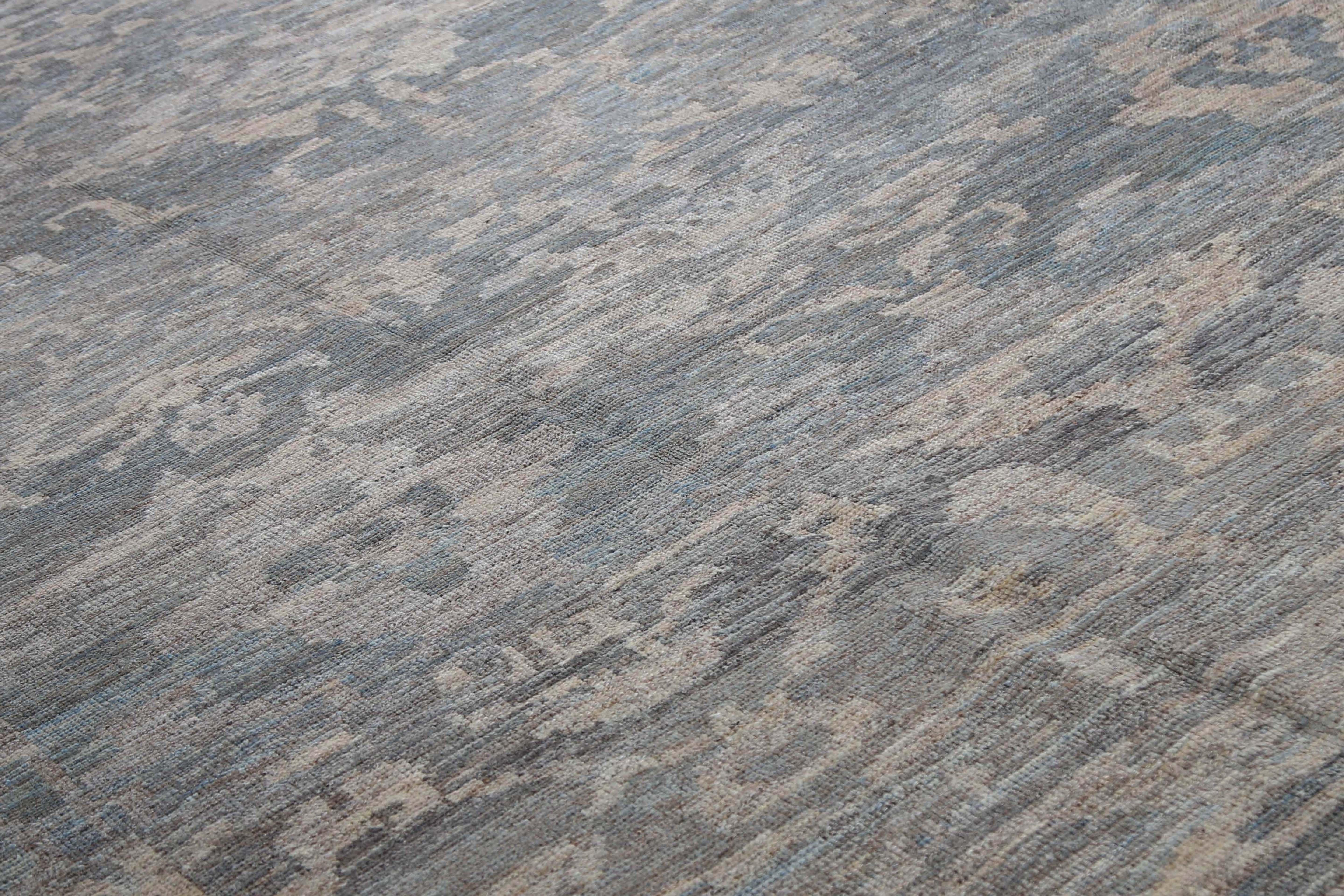 Wir präsentieren unseren handgefertigten türkischen Oushak-Teppich mit einem modernen Twist. Dieser Teppich besticht durch seine kühle Ausstrahlung mit einem dunkel blaugrauen Hintergrund, der nahtlos in das Bordürendesign übergeht. Das Design ist