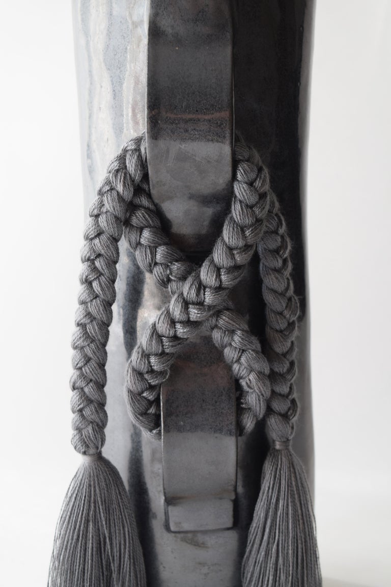 Vase #696 by Karen Gayle Tinney

Hand formed stoneware vase with black glaze. Inside is glazed black and will hold water, please take care not to damage fringe areas. A charcoal tencel braid with fringe is applied to the outside of the vase (the
