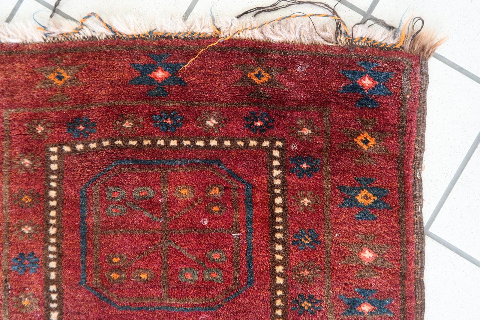 Questo tappeto afghano Baluch vintage fatto a mano, risalente agli anni '50, presenta un classico disegno geometrico tribale dalle tonalità calde e profonde. Tessuto in lana di alta qualità, presenta un ricco campo rosso accentuato da blu scuro,