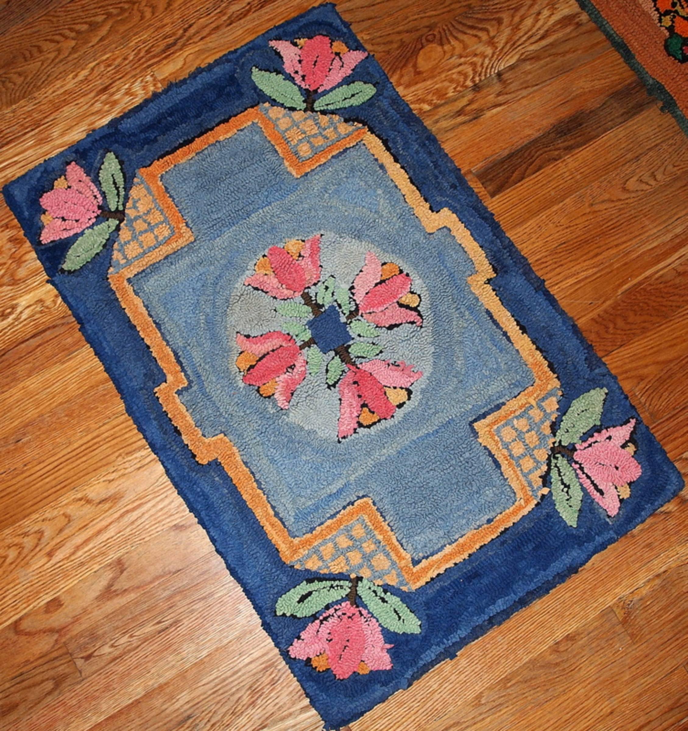 Vintage American hooked rug in combination of two different shades of blue. Dark sea blue border with pink flowers in each corner of it. Smaller inner border is in orange color and geometric shape. Sky blue field with four pink/yellow flowers in the