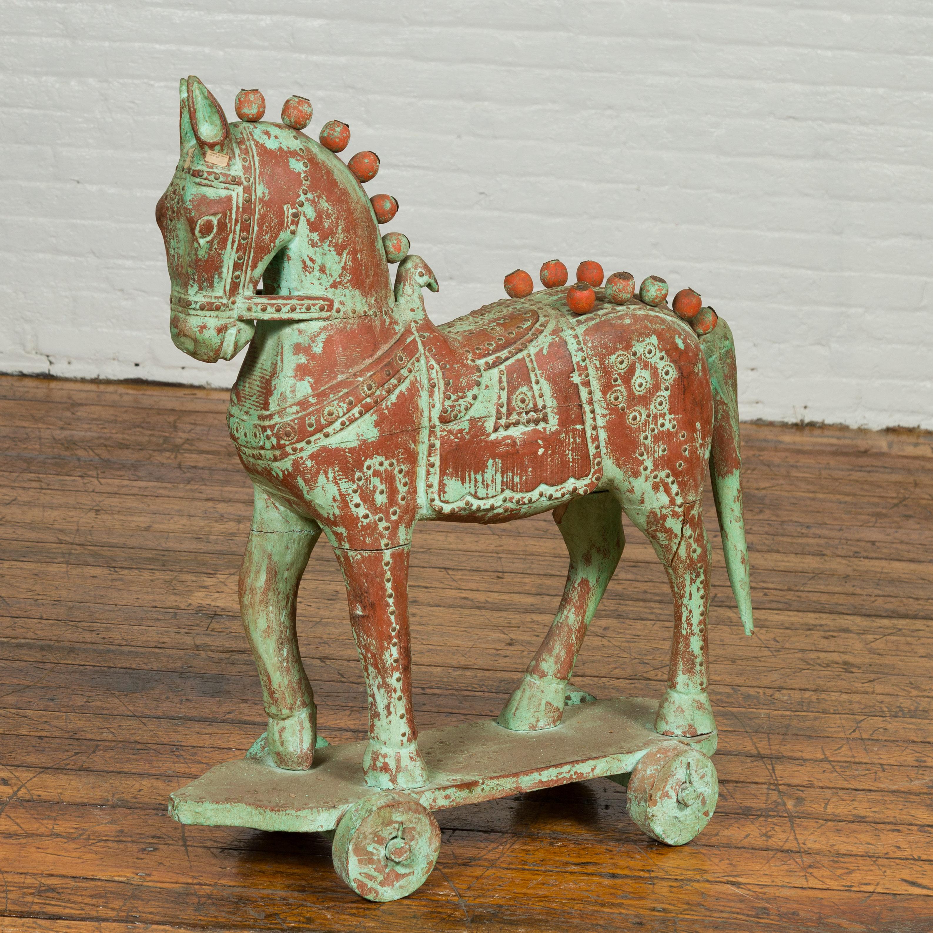 A small Indian vintage carved wooden horse sculpture from Madras with distressed rust and verdigris and iron red colored patina and petite spheres. Born in the Indian state of Tamil Nadu during the midcentury period, this carved horse charms us with