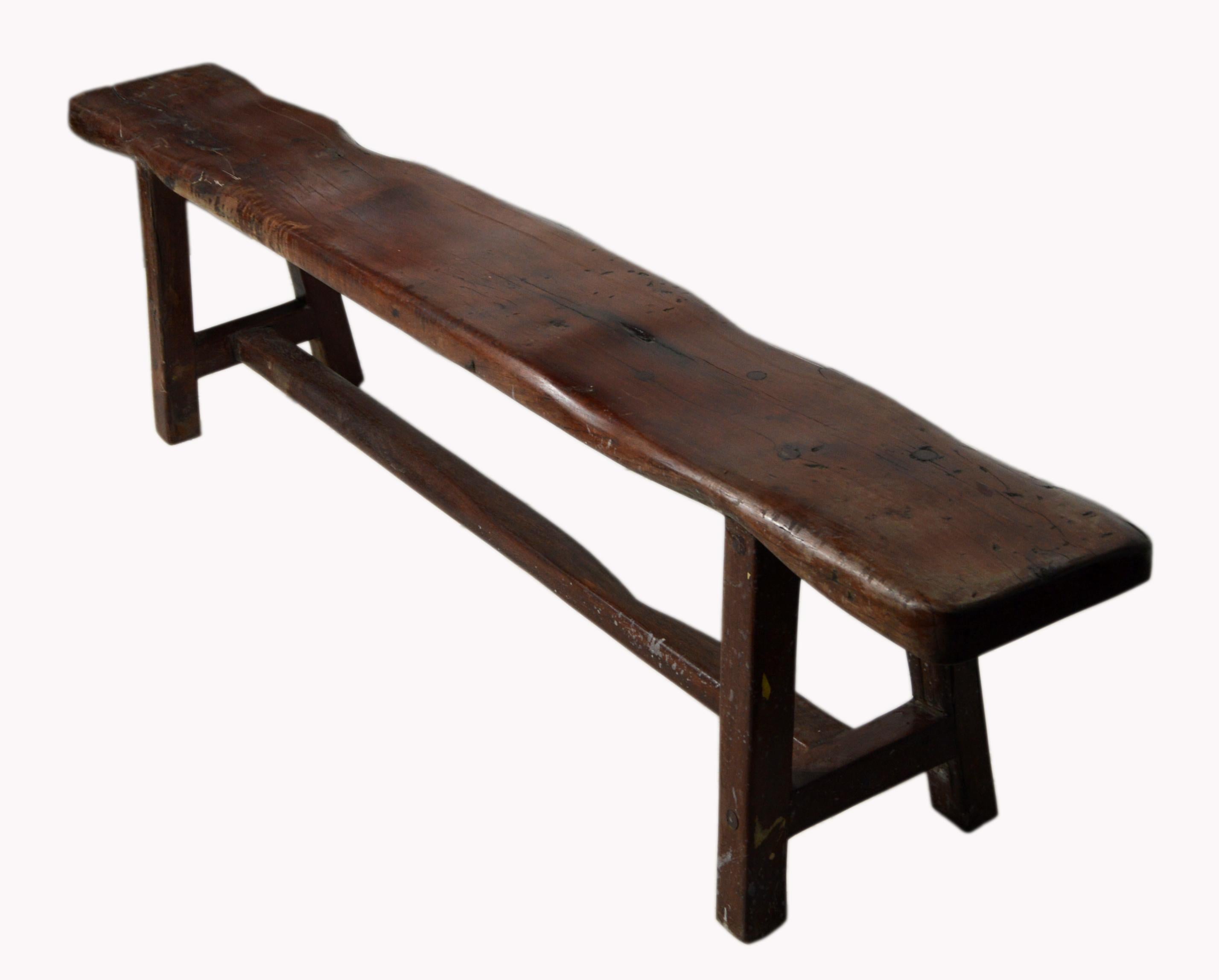 A handmade vintage Javanese long rustic wooden bench with brown finish. Born in the Indonesian island of Java during the mid 20th century, this narrow bench features a charming long and tick rectangular seat resting on four slightly splayed legs,