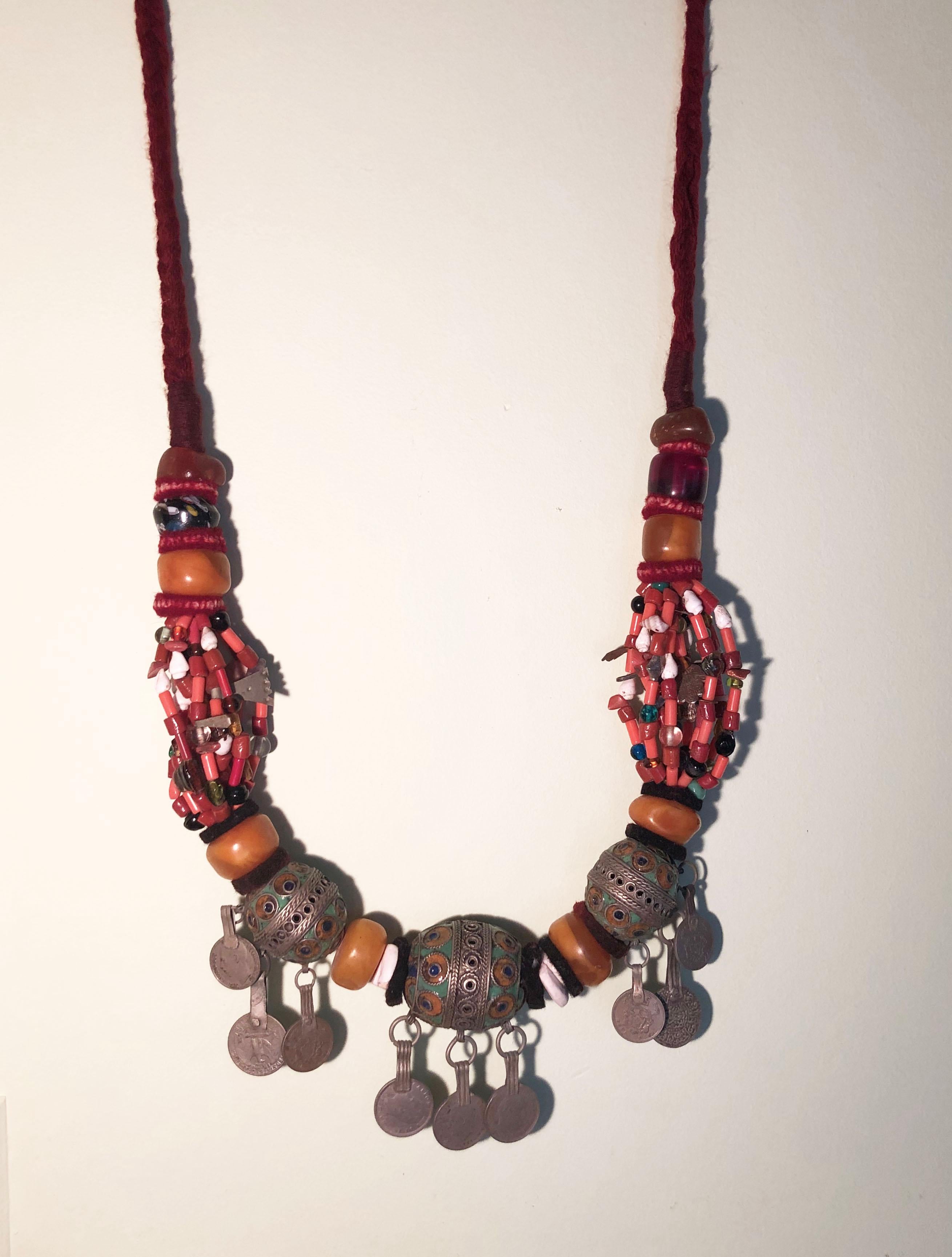 Handmade artisan pendant necklace from Morocco. Made in the southern desert town of Zagora, this necklace has many precious beads including coral, glass, amber copal resin, shells, onyx, and more. Numerous silver charms & hamsa hand of fatima good