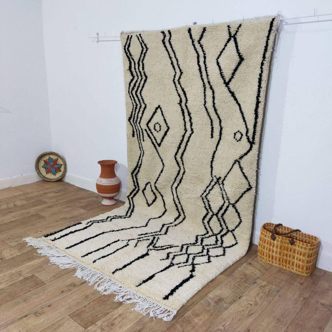 Dieser handgefertigte marokkanische Berberteppich im Vintage-Stil aus den 1980er Jahren zeigt die reiche Tradition der Berberweberei mit kühnen geometrischen Mustern und Zickzack-Mustern auf einem warmen beigen Wollgrund. Die filigranen schwarzen