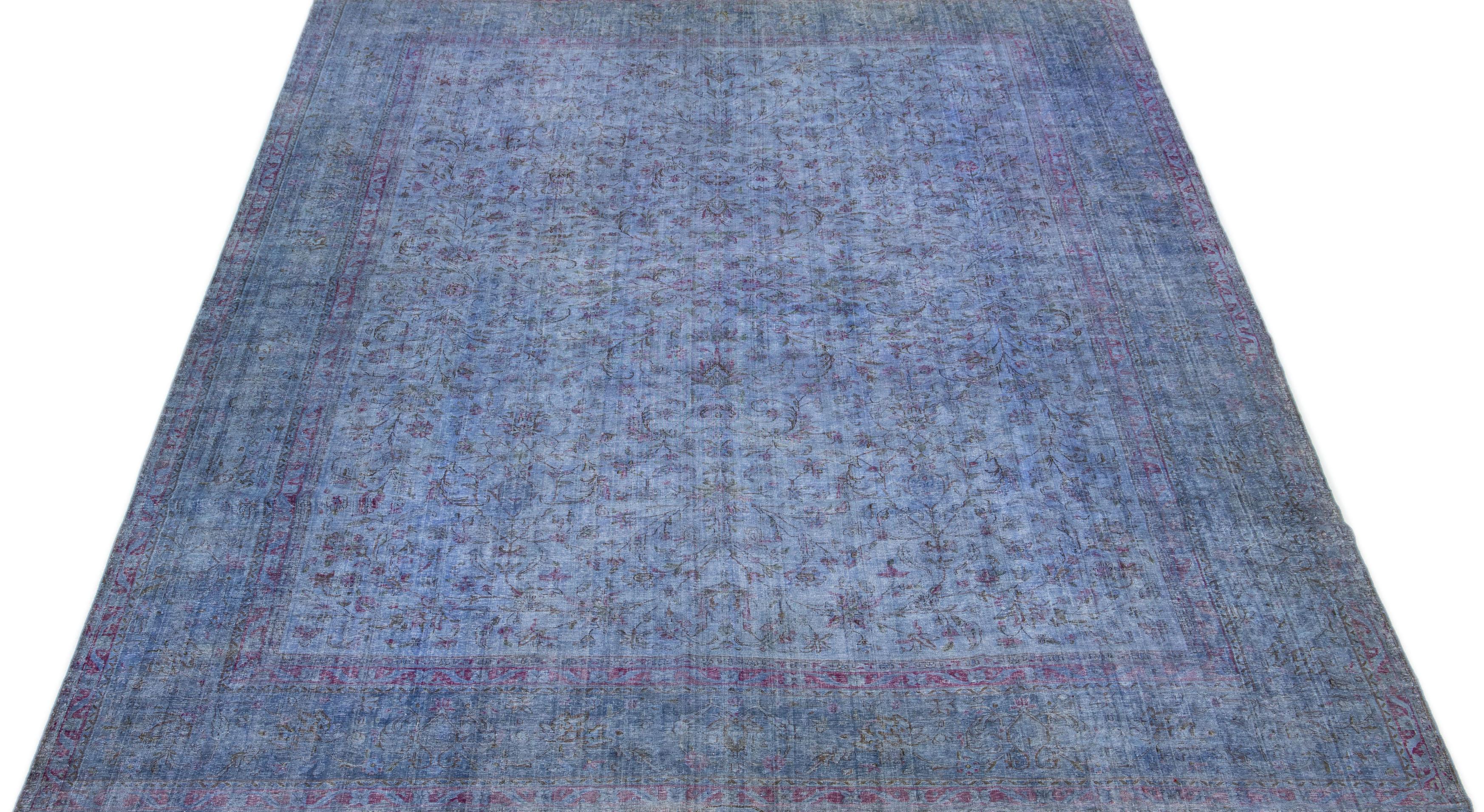 An extensive floral pattern embellishes the center of this Persian rug from the 1950s, which has been intentionally aged and overdyed to achieve a rustic appearance. The rug's great blue color adds a refined and sophisticated touch to any