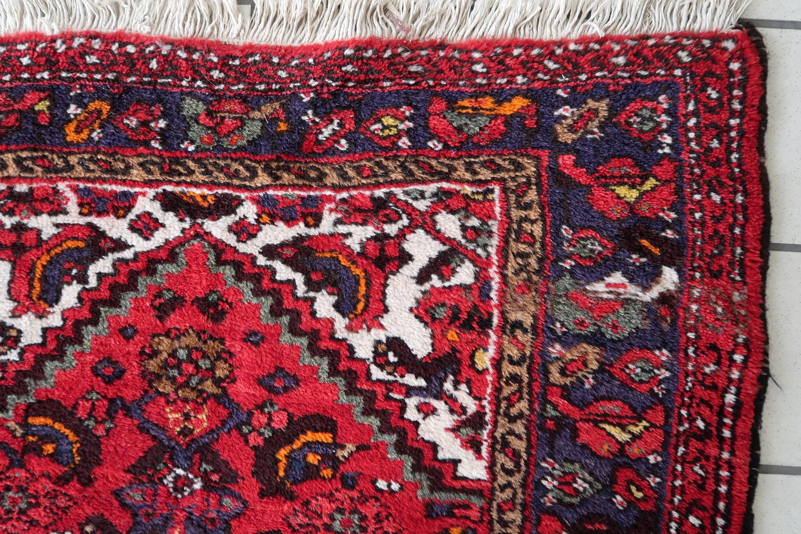 Questo tappeto persiano Hamadan vintage fatto a mano degli anni '70 presenta un sorprendente campo rosso ornato da intricati motivi floreali e geometrici in toni profondi e contrastanti. Il disegno è incorniciato da un ricco bordo blu navy con