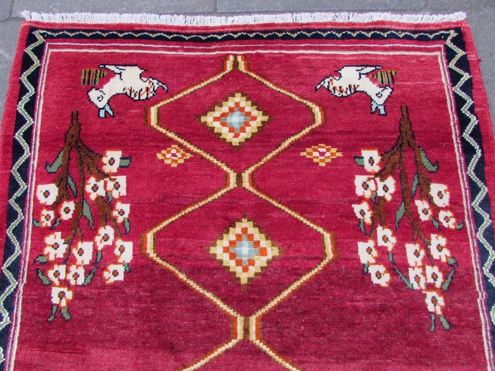 Mit diesem handgefertigten roten Gabbeh-Teppich im persischen Vintage-Stil verleihen Sie Ihrem Zuhause einen Hauch von traditionellem Charme. Dieser in den 1970er Jahren gefertigte Teppich zeigt einen leuchtend roten Hintergrund, der mit skurrilen