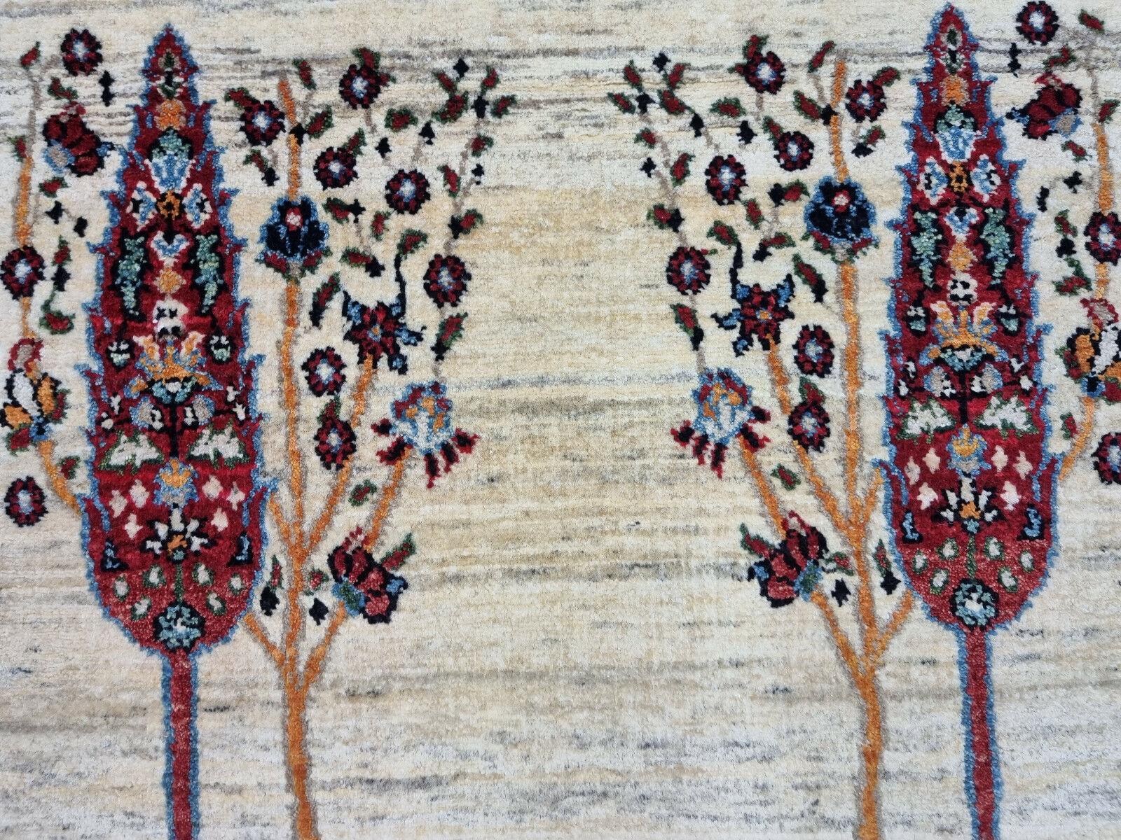 Design: This handmade rug features an artistic representation of trees and foliage motifs. The design exudes a vintage charm.
Colors:
Base: The background color is a faded beige, contributing to its vintage appearance.
Tree Motifs: Prominent tree