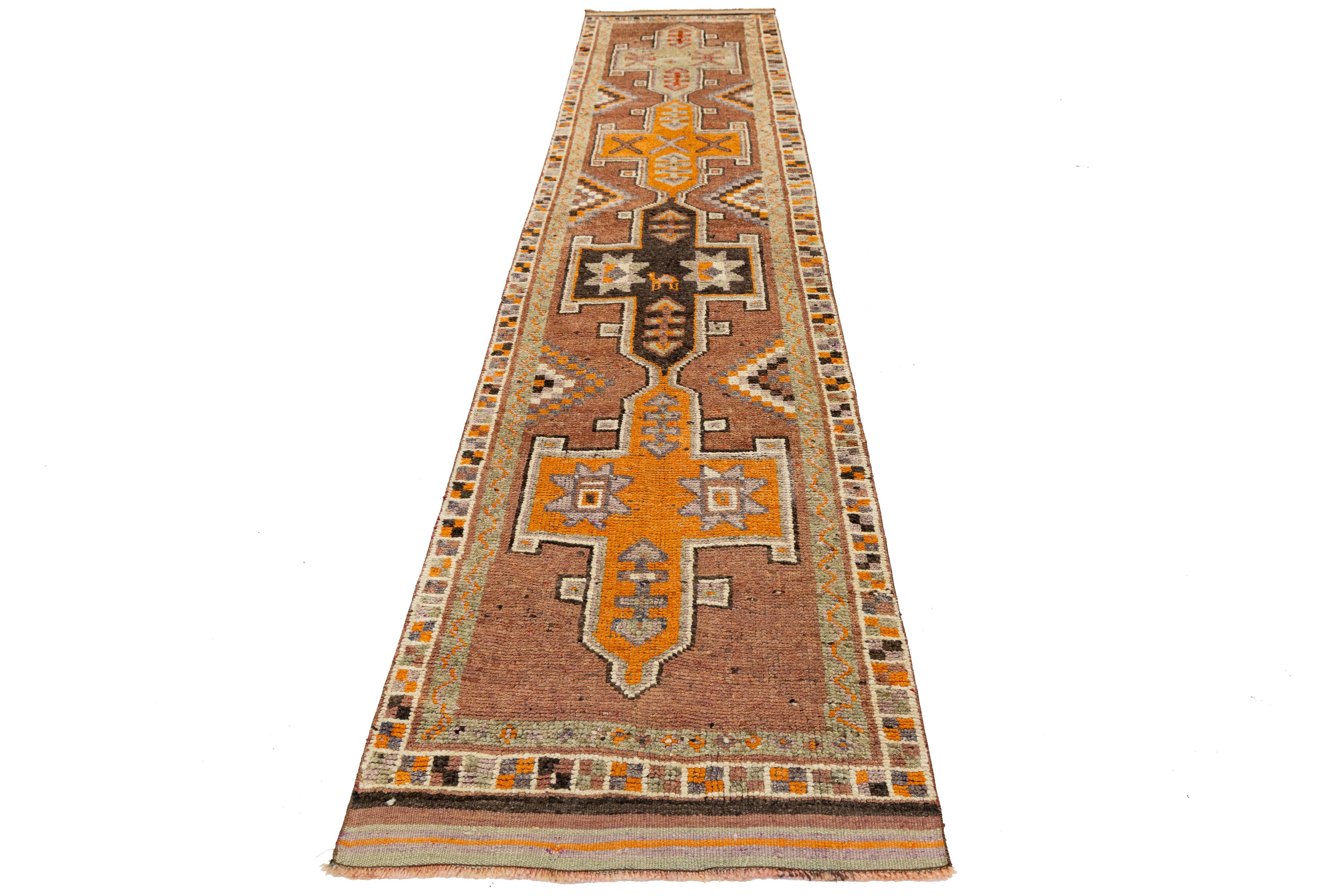 Dieser in der Türkei handgewebte Vintage-Läufer zeigt kühne geometrische Muster und stilisierte Sternformen in warmen Braun-, Orange- und Goldtönen. Inspiriert von der traditionellen anatolischen Weberei, bieten das längliche Format und die