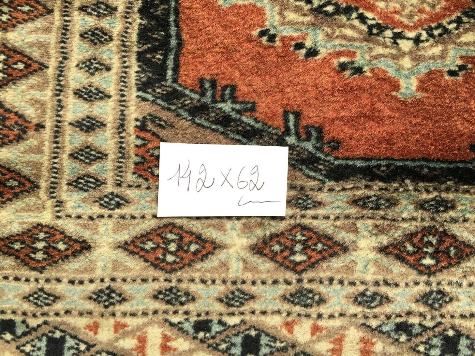 This Handmade Vintage Uzbek Bukhara Rug is a captivating piece crafted in the 1960s. Measuring 2’ x 4.6’ (62cm x 142cm), it boasts intricate craftsmanship and vibrant colors. Let’s explore its features based on the image:

Colors and Patterns:
The