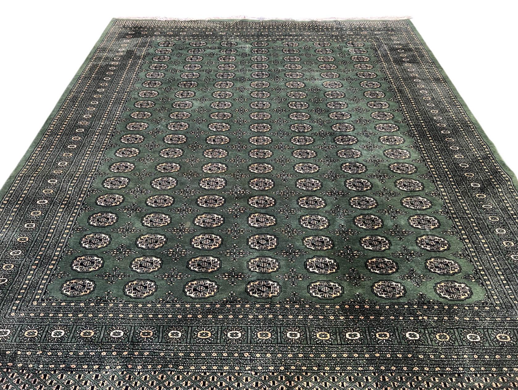 A handmade, vintage Uzbek Bokhara rug in dark green in the traditional design. Bokhara rugs fall into the  Oriental rug category that has existed for centuries. These rugs are known for their unique geometric designs and vibrant colors, and they